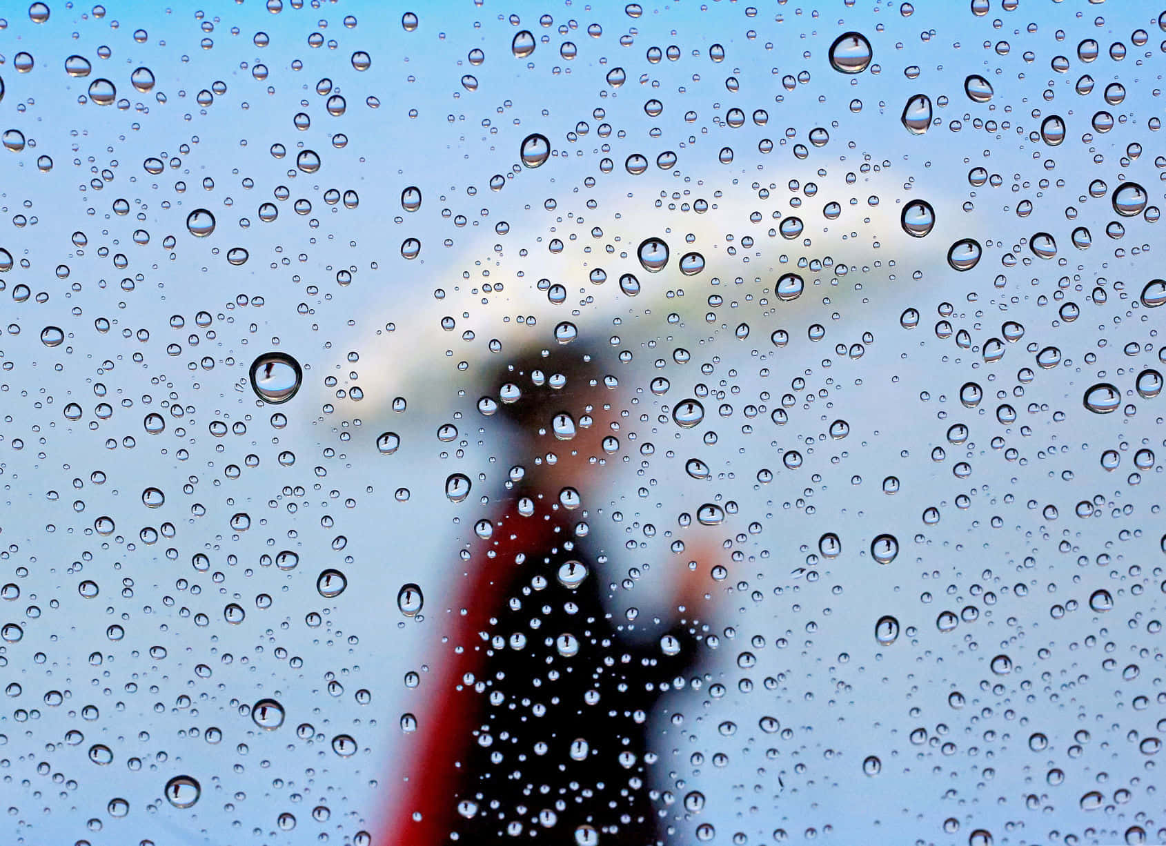透過濺滿雨水的窗戶看到模糊的人撐著雨傘