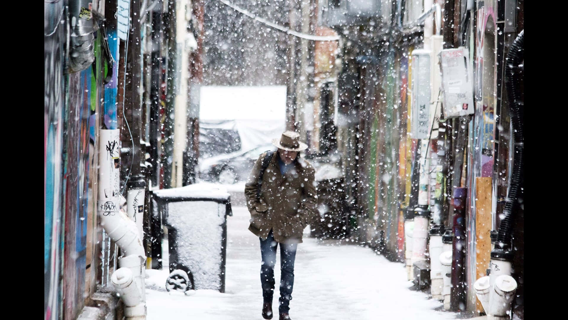 人在雪中走過佈滿塗鴉的都市小巷。