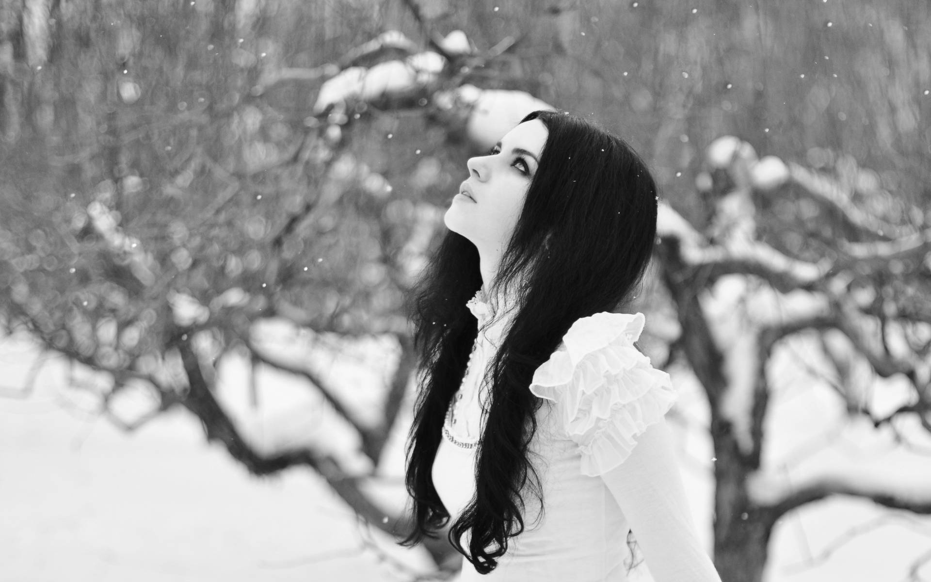 白色連衣裙女性在冬日森林中仰望飄雪。