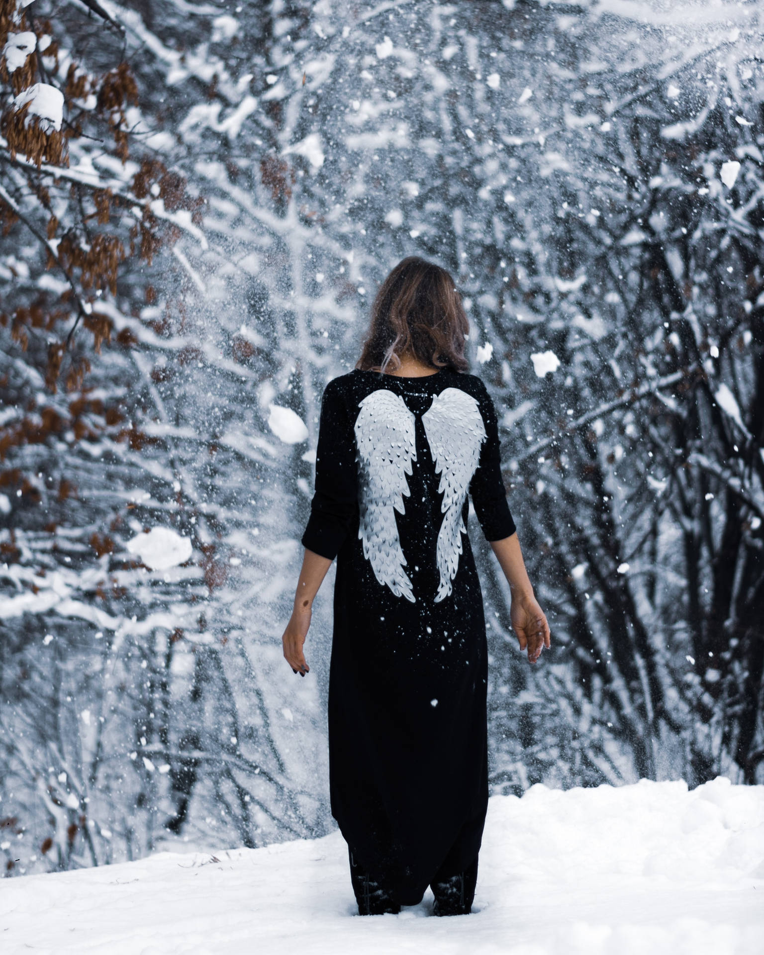擁有天使翅膀的女性在雪地森林中行走