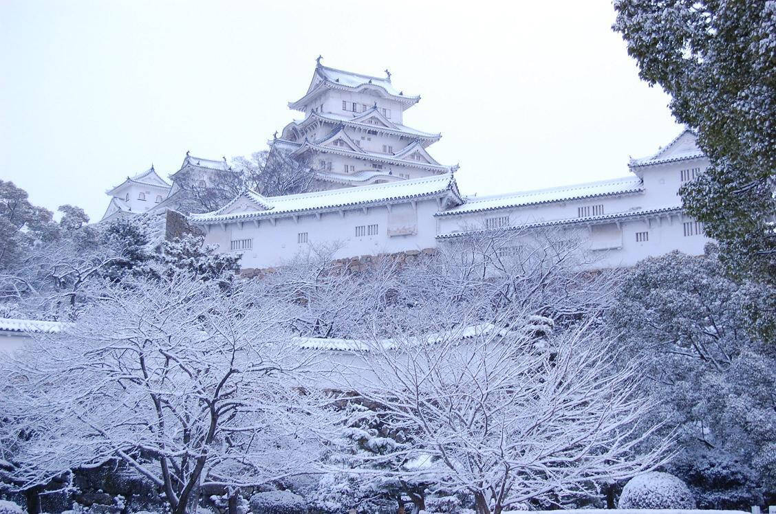 一座歷史悠久的日本城堡被白雪覆蓋，前景是積雪的樹木。