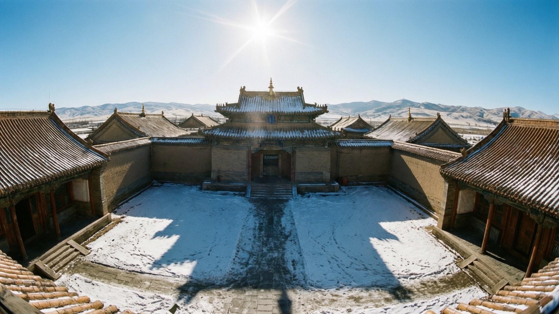 陽光照射的傳統寺廟庭院被雪覆蓋，背景有山巒。