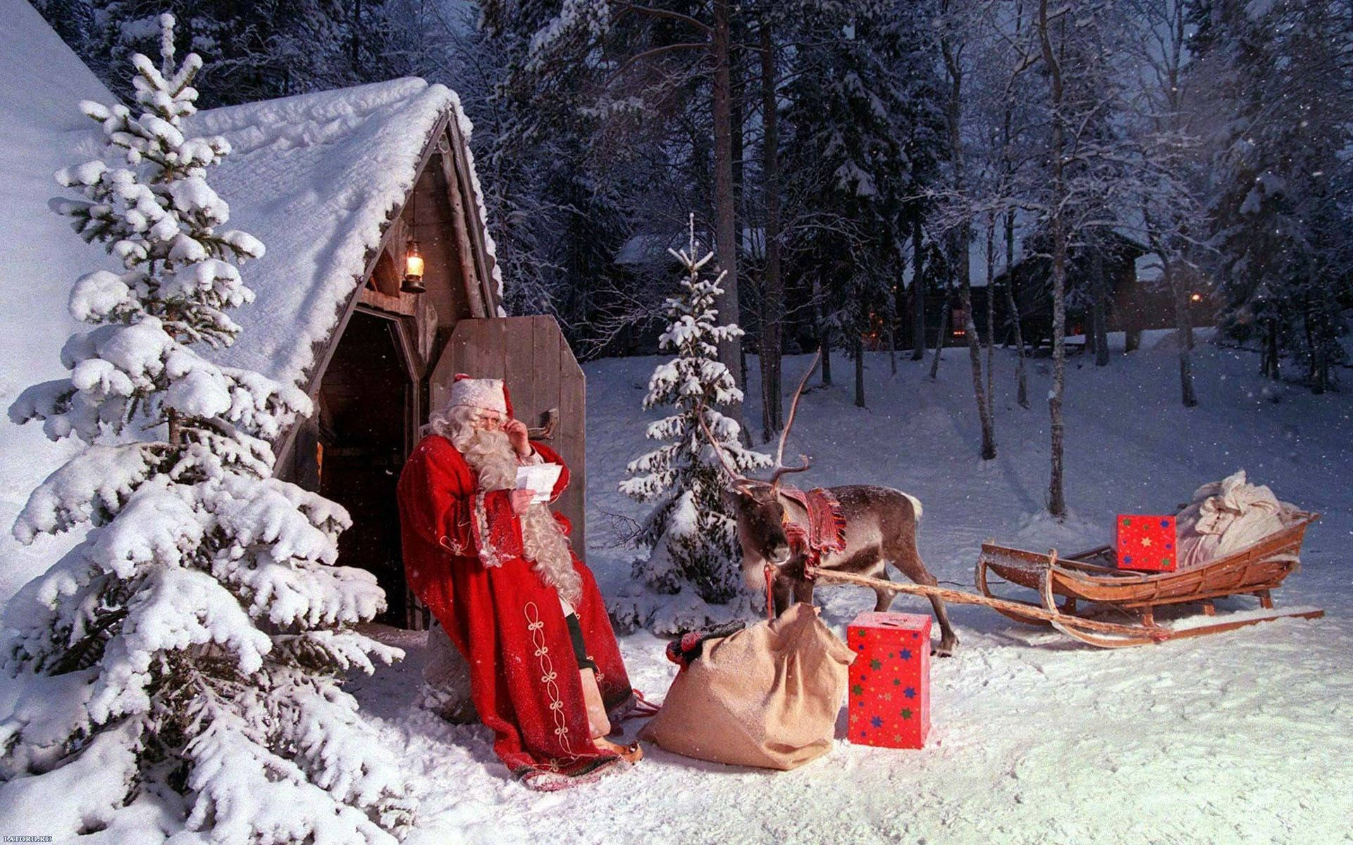 雪中木屋聖誕節桌面壁紙 壁紙 — 聖誕老人身穿紅色長袍，在黃昏的冬季森林中，站在一間被雪覆蓋的小屋外，旁邊有一隻馴鹿和雪橇。