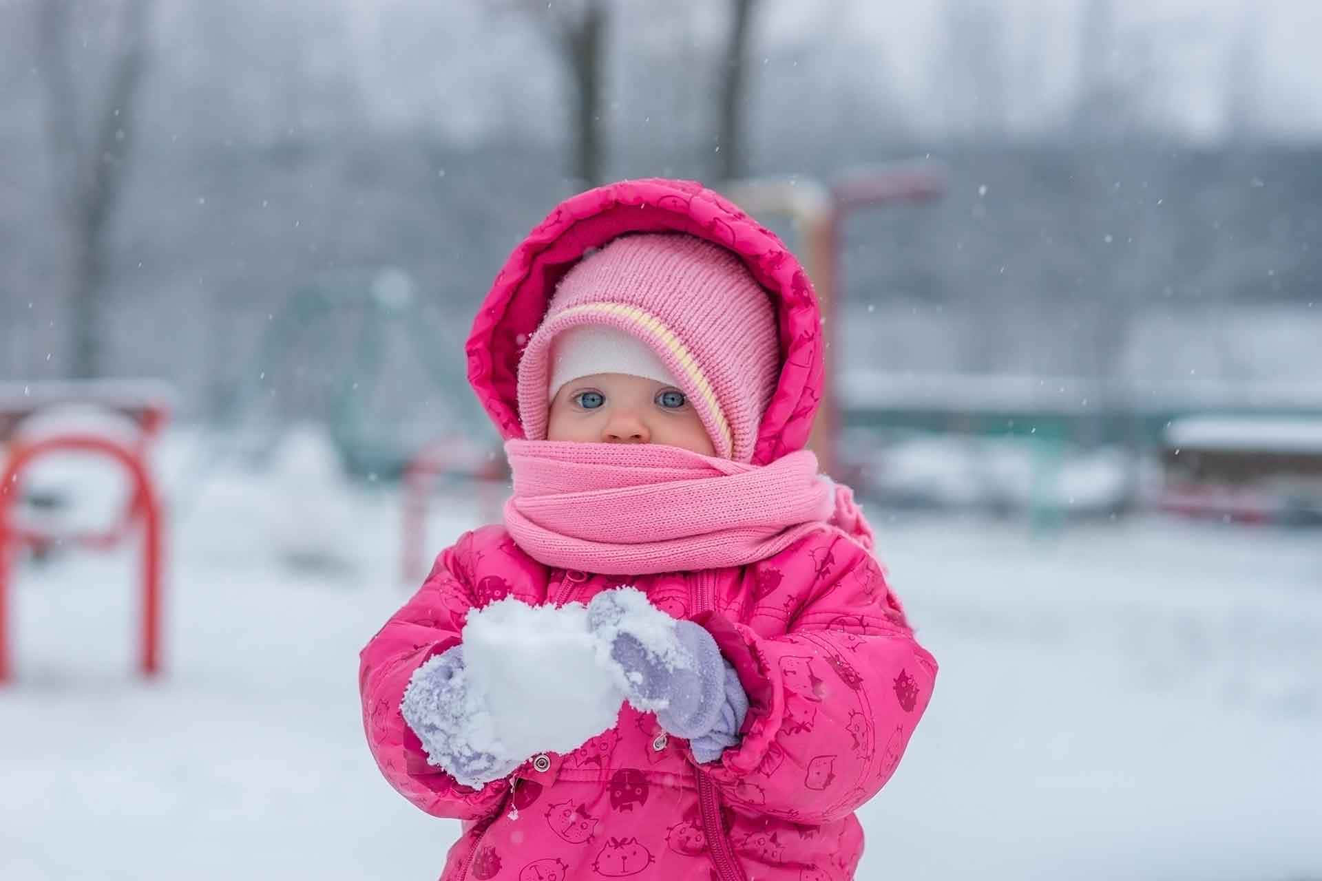 穿著粉紅色冬季裝備的小孩在雪地公園裡拿著雪球