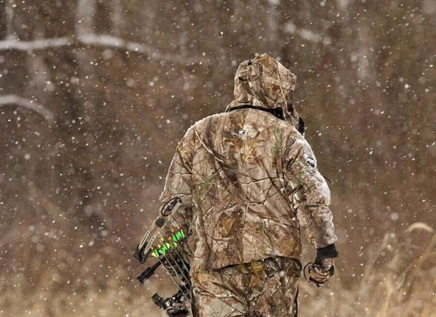 身穿迷彩裝備的獵人在雪林裡拿著弓行走。