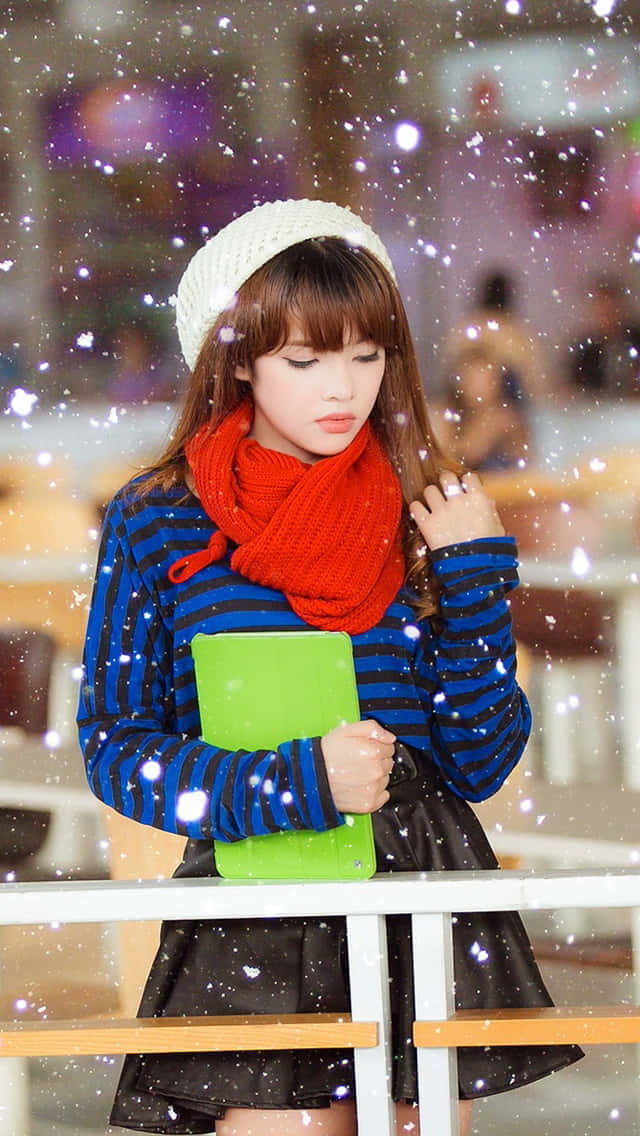 年輕女子穿著冬季服裝，在室內下雪時手持一本書。