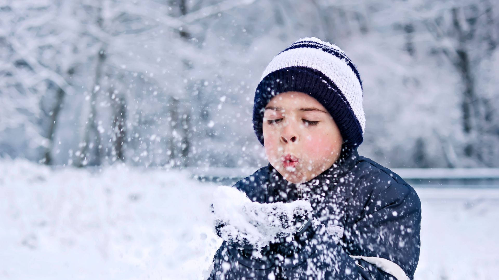 孩子在冬季森林中戴著條紋冷帽和手套吹雪