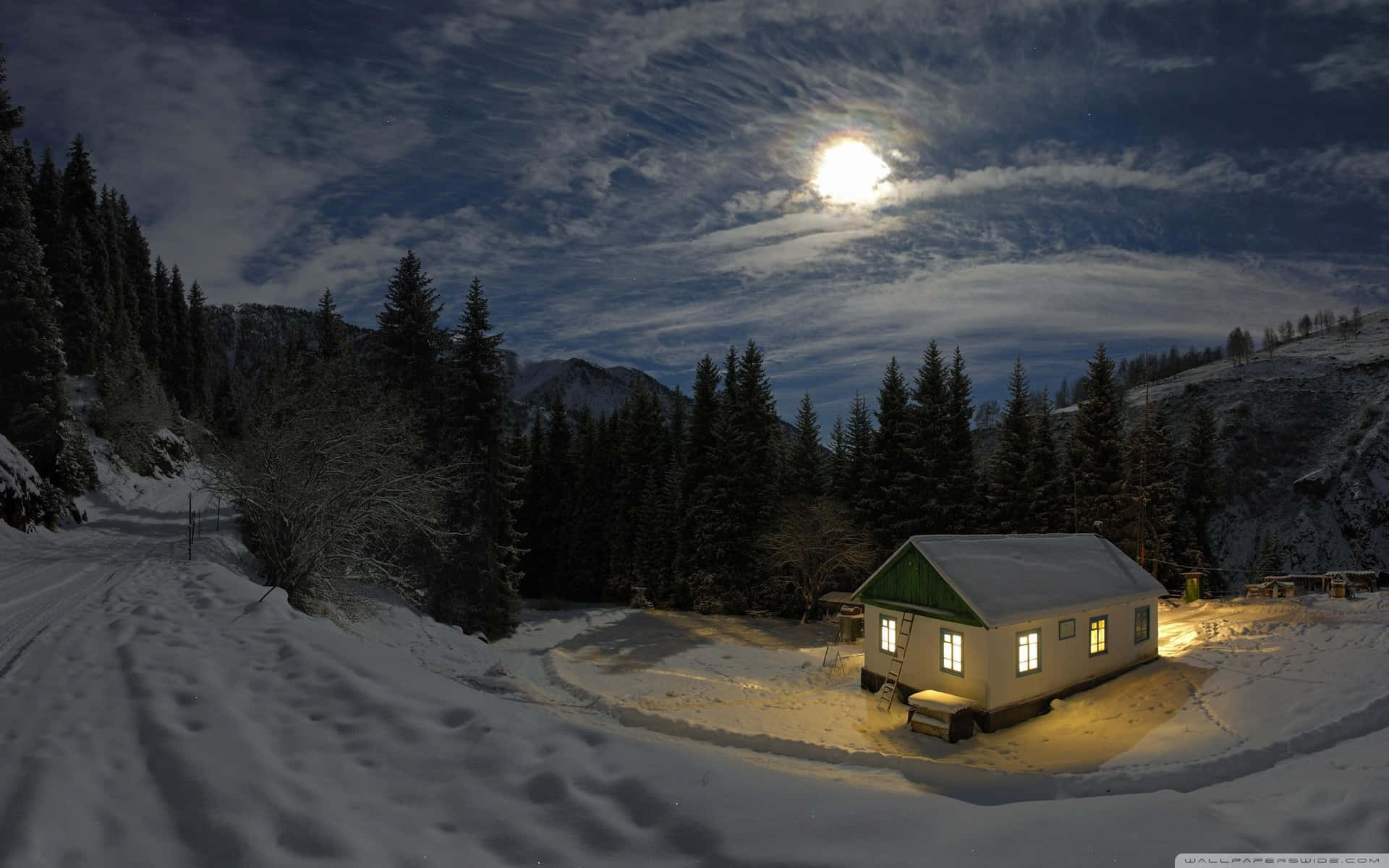在明亮的月光下，雪地冬季森林中溫暖照明的小屋。