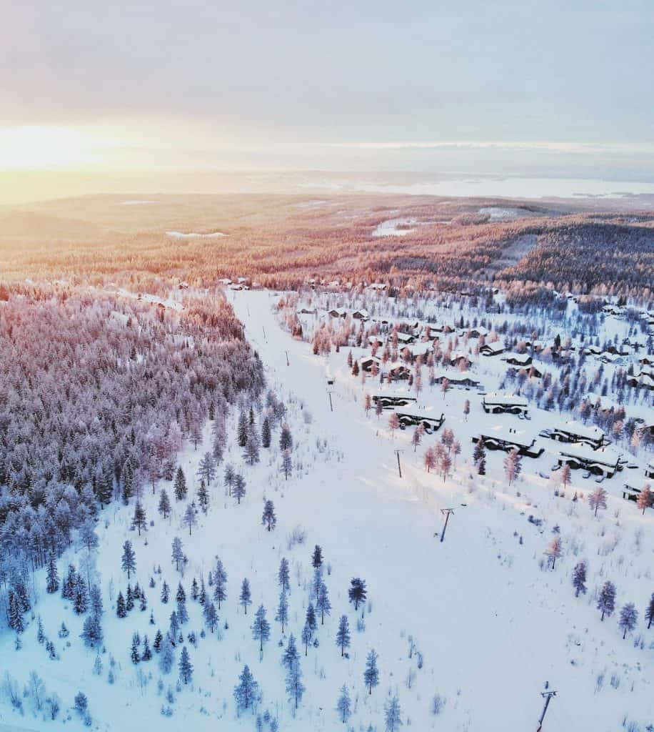 雪原日出空中攝影 壁紙 — 金色日出時，位於森林山谷中的雪地滑雪勝地鳥瞰圖。