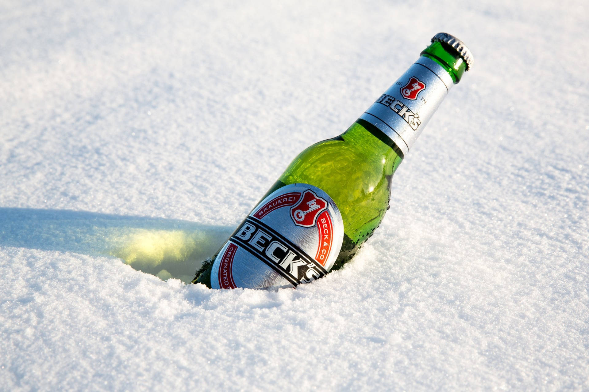 一個冰凍嘅Beck's啤酒樽放在新鮮雪中，喺明亮陽光下。
