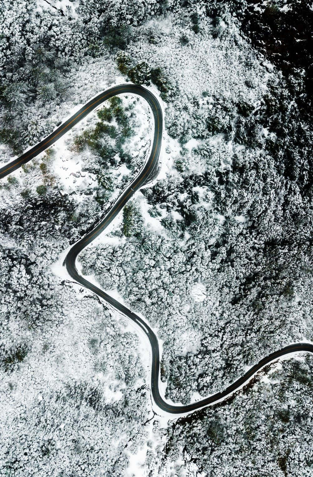 雪地道路空中視角原版 iPhone 5s 壁紙 — 一條蜿蜒的道路從空中俯瞰穿過白雪覆蓋的森林。