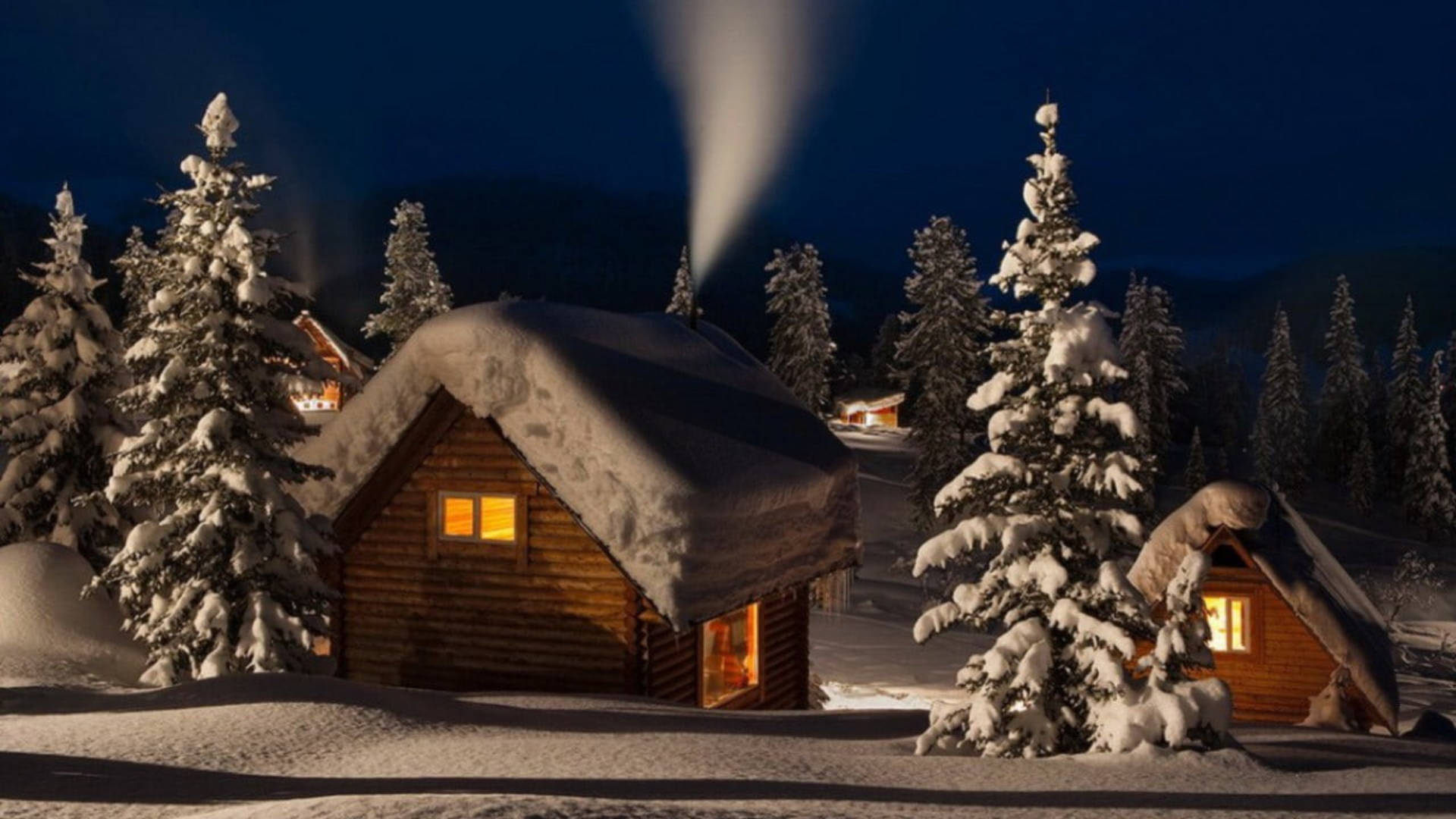雪夜溫馨木屋 壁紙 — 被雪覆蓋的木屋在夜空下被霜凍的松樹環繞，溫暖地發光。