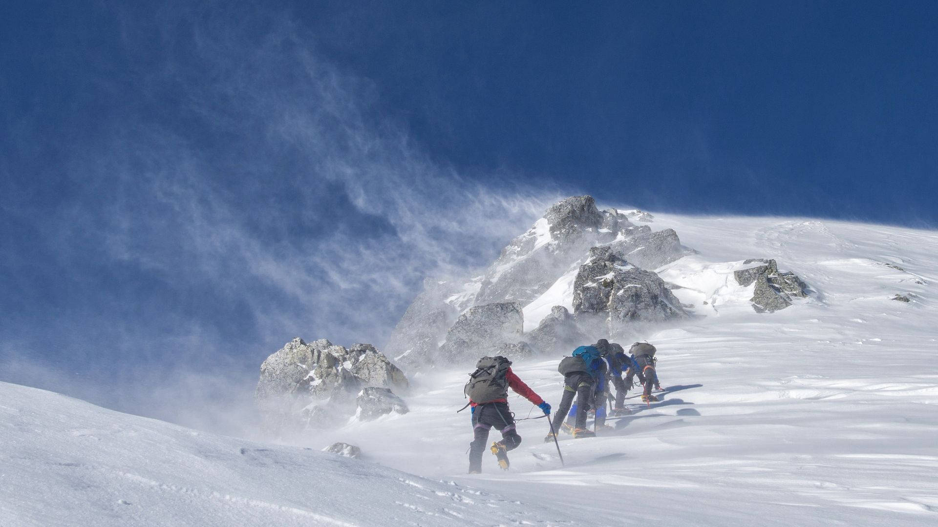 四位登山者在有風的條件下走在積雪的山坡上。