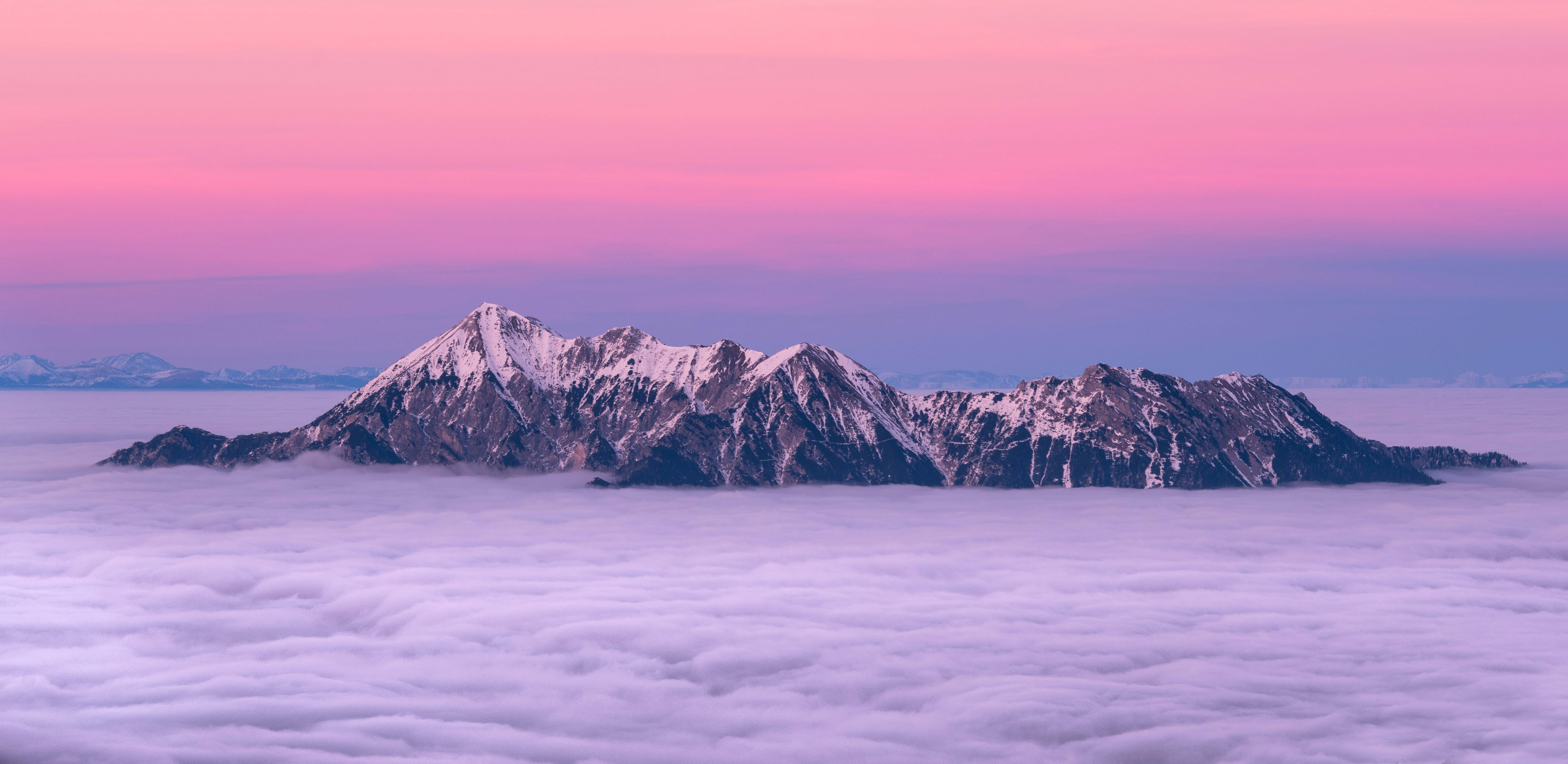 雪山之上粉紅天空 Mac 4K 壁紙 — 白雪覆蓋的山峰在暮色中雄偉地聳立在柔和的紫色雲海之上。