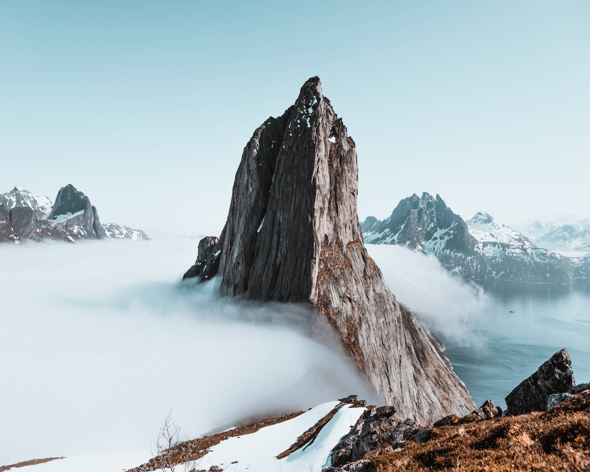 一座戲劇性的山峰聳立於雲層之上，頂部積雪，下方有水。