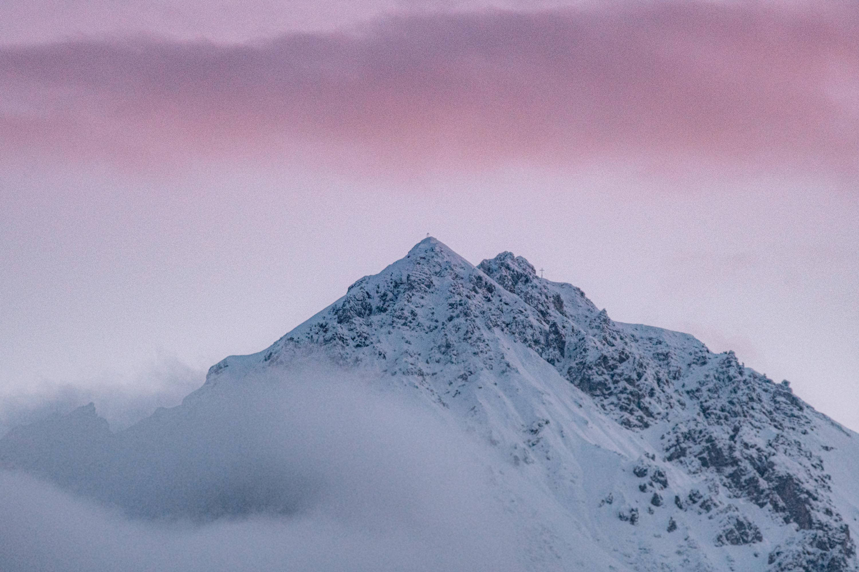 雪山峰頂冬季桌面 壁紙 — 一座積雪的山峰在薄霧中升起，伴隨著黎明時分柔和的粉紅色和紫色天空。