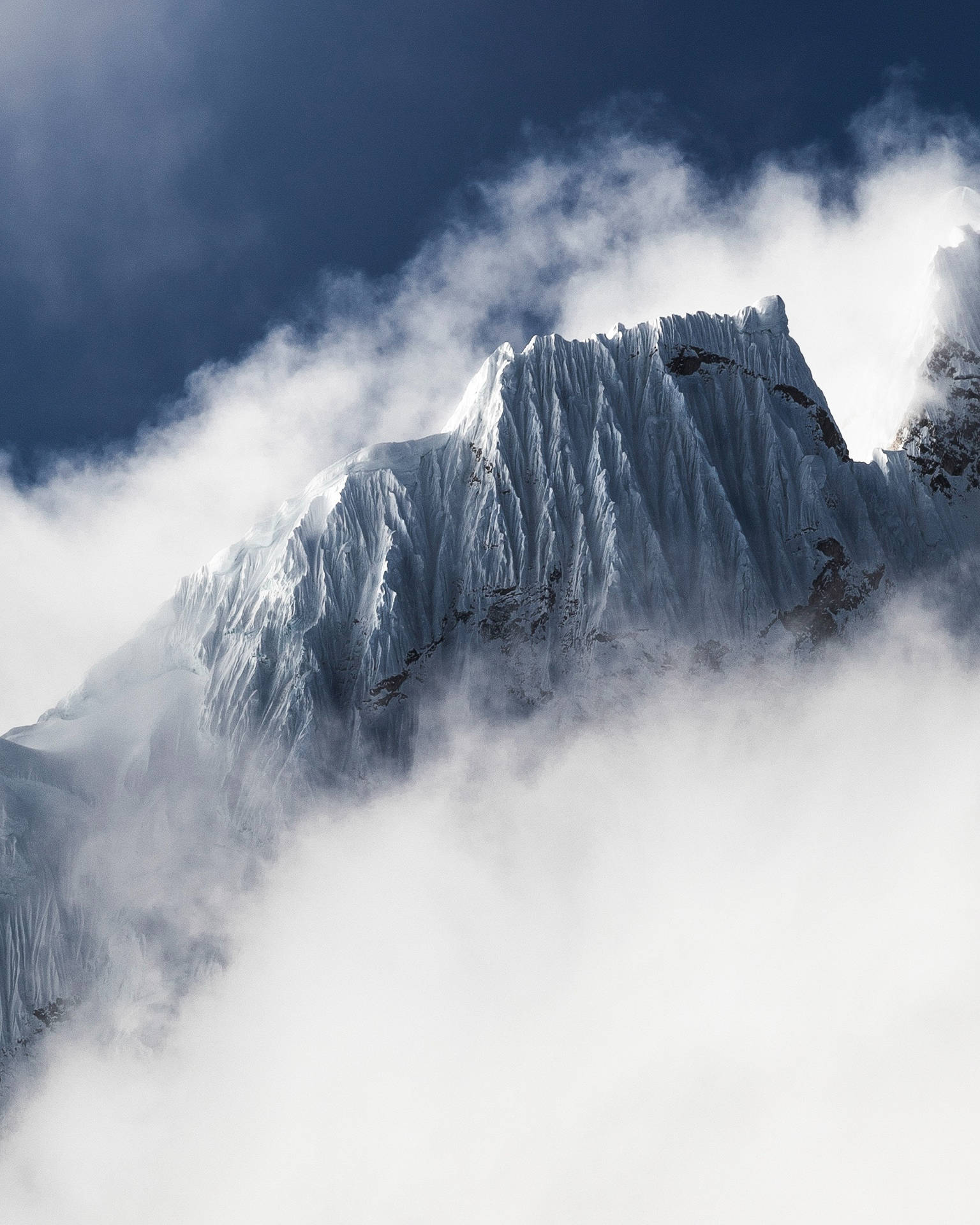 積雪山峰在深藍色天空的雲層之上聳立