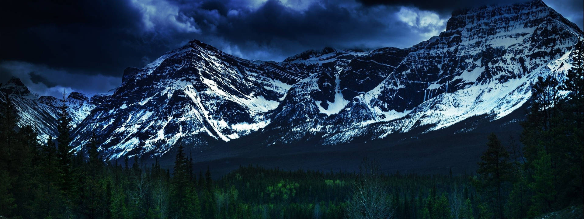 暴風雨夜空下的雪山，前景有松樹