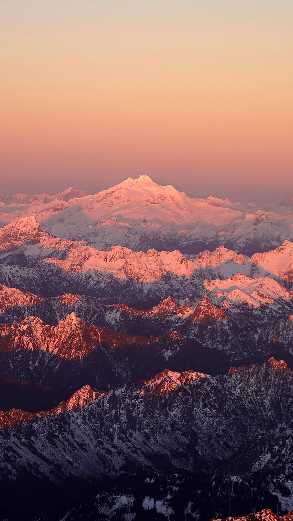 雪山自然 iPhone 背景 壁紙 — 在日出或日落期間，白雪覆蓋的山峰沐浴在溫暖的粉紅色和橙色色調中的令人嘆為觀止的空中景觀。