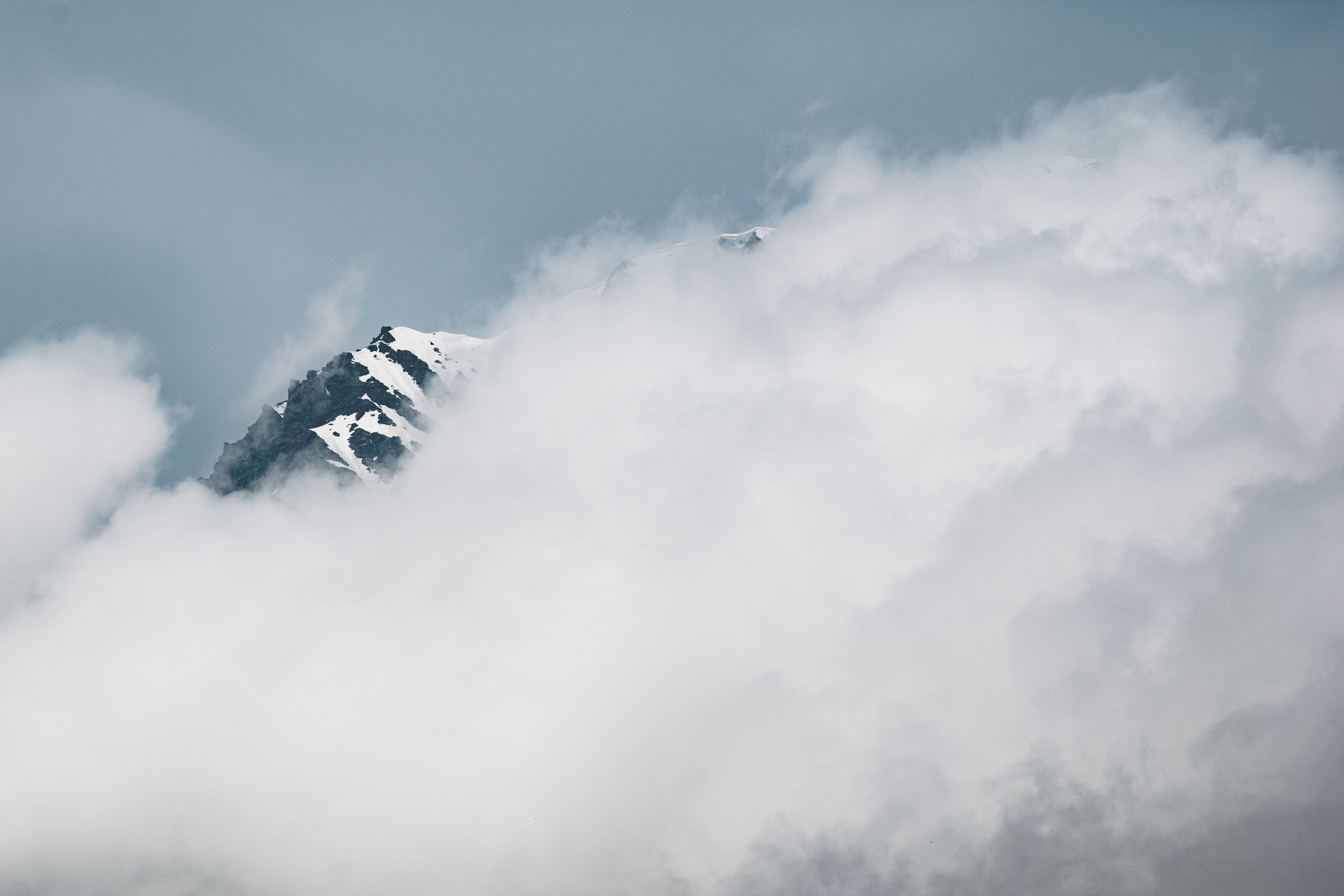 雪山頂安卓平板壁紙 壁紙 — 白雪覆蓋的山峰在灰濛濛的天空下，從翻滾的白雲中戲劇性地顯現出來。