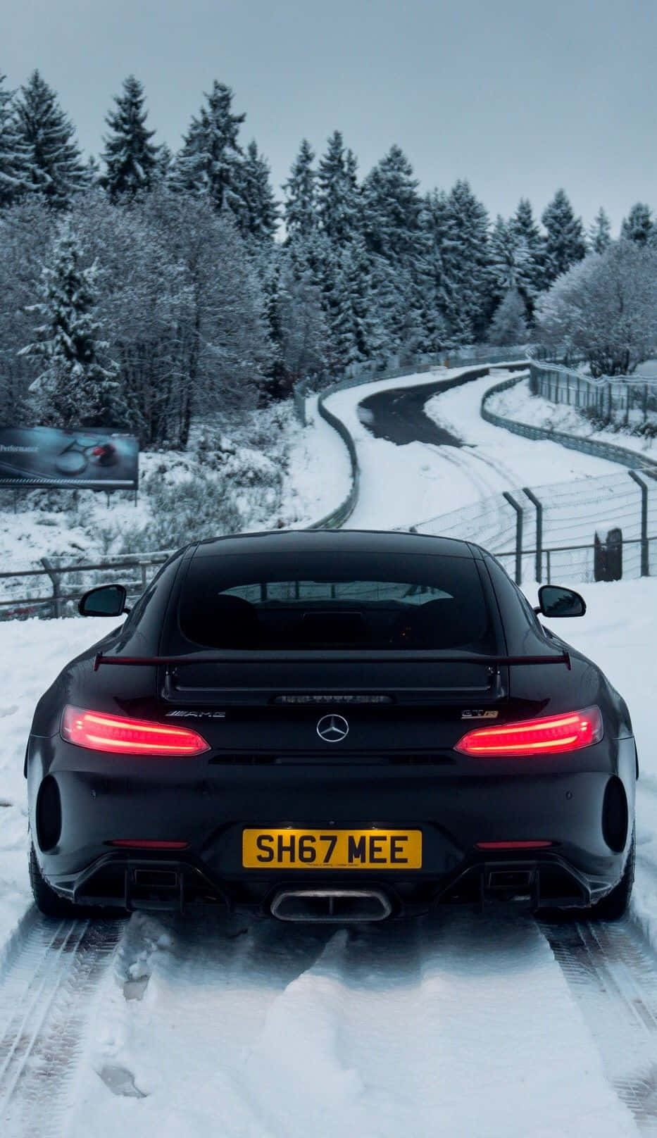 雪山黑AMG GT-R安卓背景 壁紙 — 一輛黑色平治AMG GT R，亮著紅色尾燈，在黃昏時分駛過白雪覆蓋的森林道路。