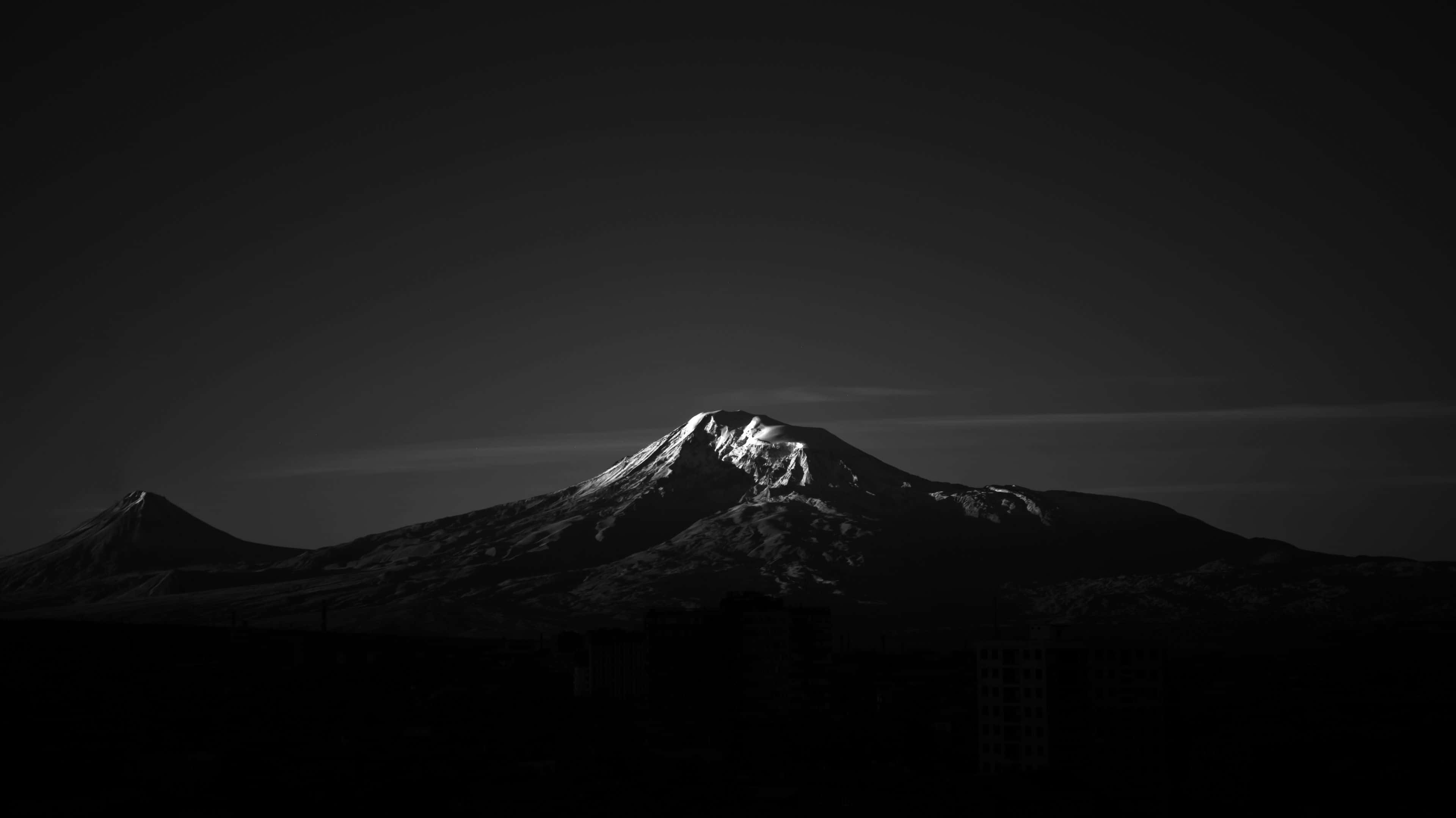 雪峰山巒 AMOLED 桌面 壁紙 — 一個鮮明的黑白山峰剪影，雪覆蓋的山頂在黑暗的天空中閃耀。
