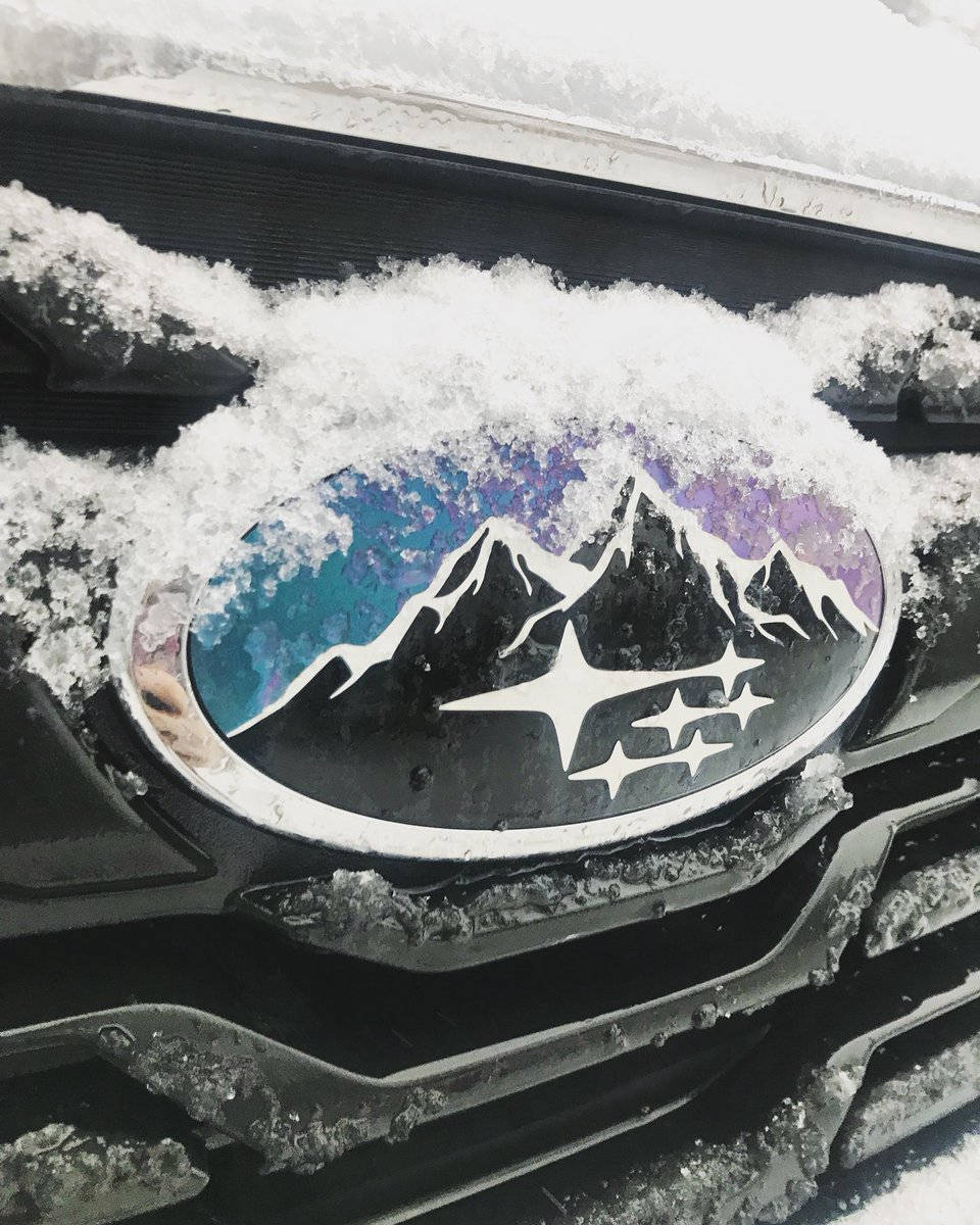 雪景中的修改版斯巴魯標誌 壁紙 — 黑色車頭蓋上沾滿雪的Subaru標誌，呈現紫色和藍色天空下帶有白色星星的山脈。