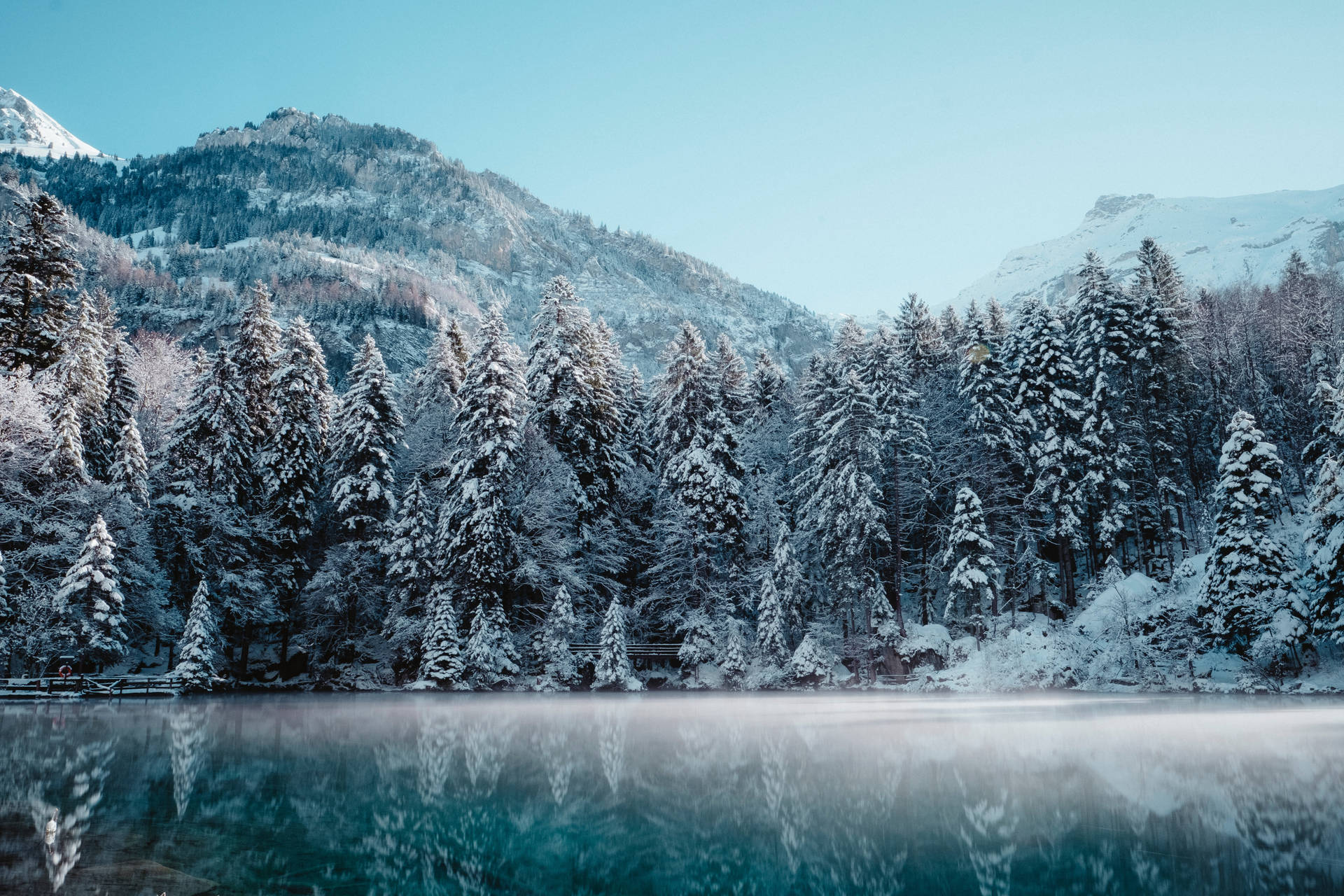 白雪覆蓋的樹木和山脈倒映在平靜的湖水中，天空清澈湛藍。