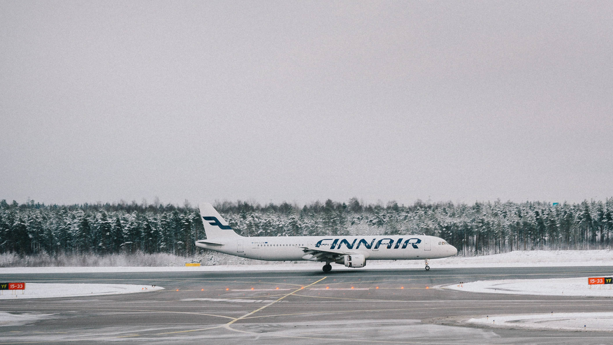 雪景機場跑道 壁紙 — 一架芬蘭航空的飛機停在灑滿雪的跑道上，背景是白雪覆蓋的樹林和陰天。