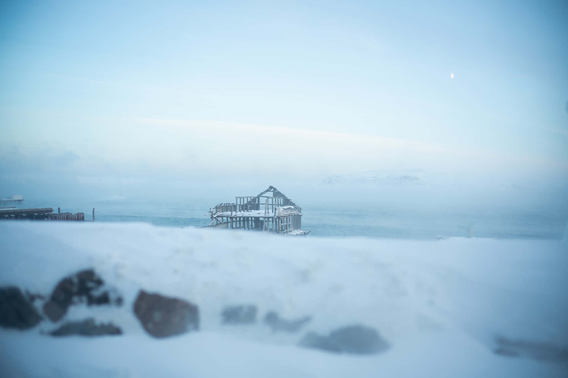 被遺棄的雪覆蓋碼頭，在霧濛濛的冬日大海中，淡藍色天空和可見的月亮。