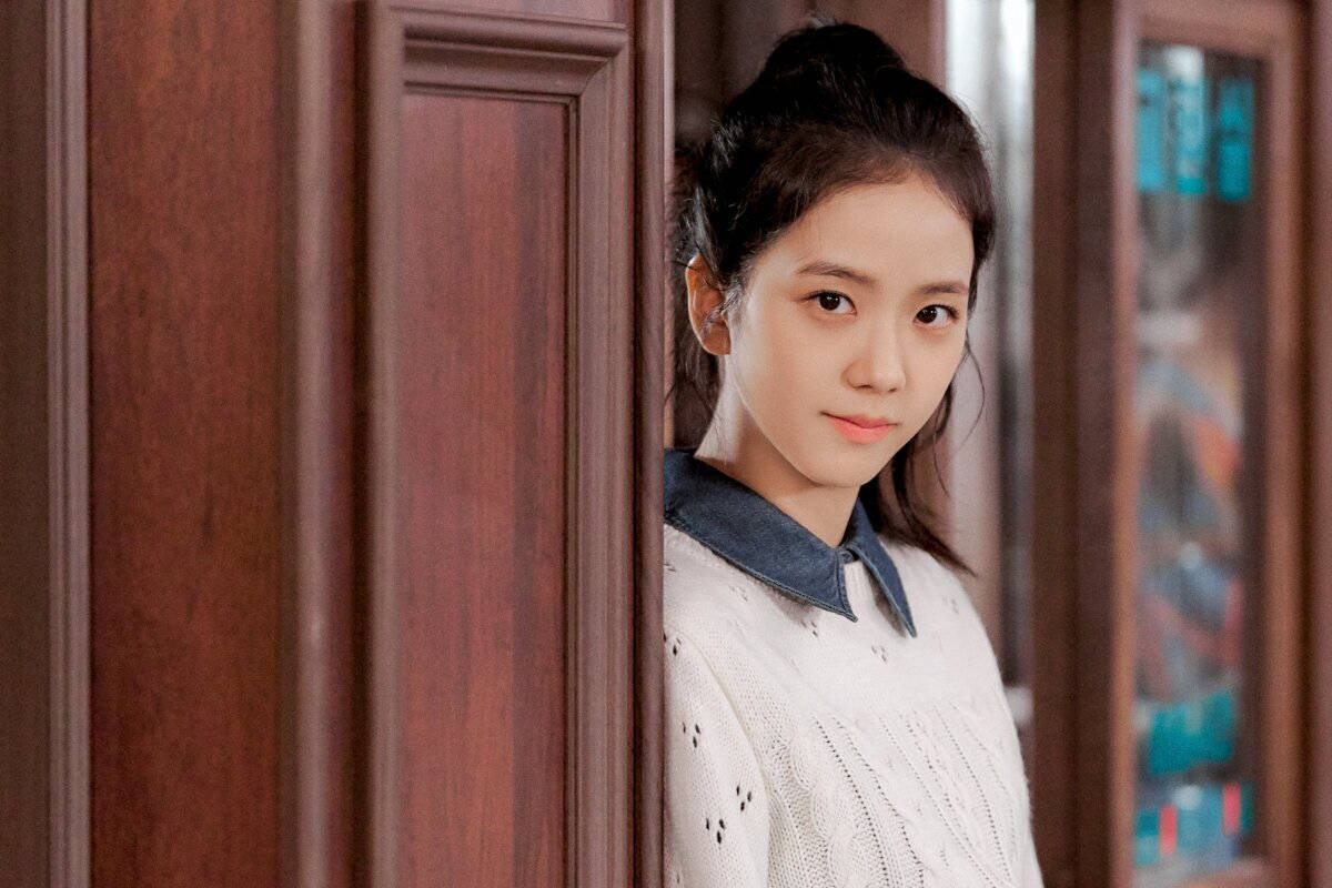 《雪滴花》劇中Eun Yeong-ro 壁紙 — 一位深色頭髮的年輕女子從木門後探頭，身穿白色針織毛衣配牛仔布領。