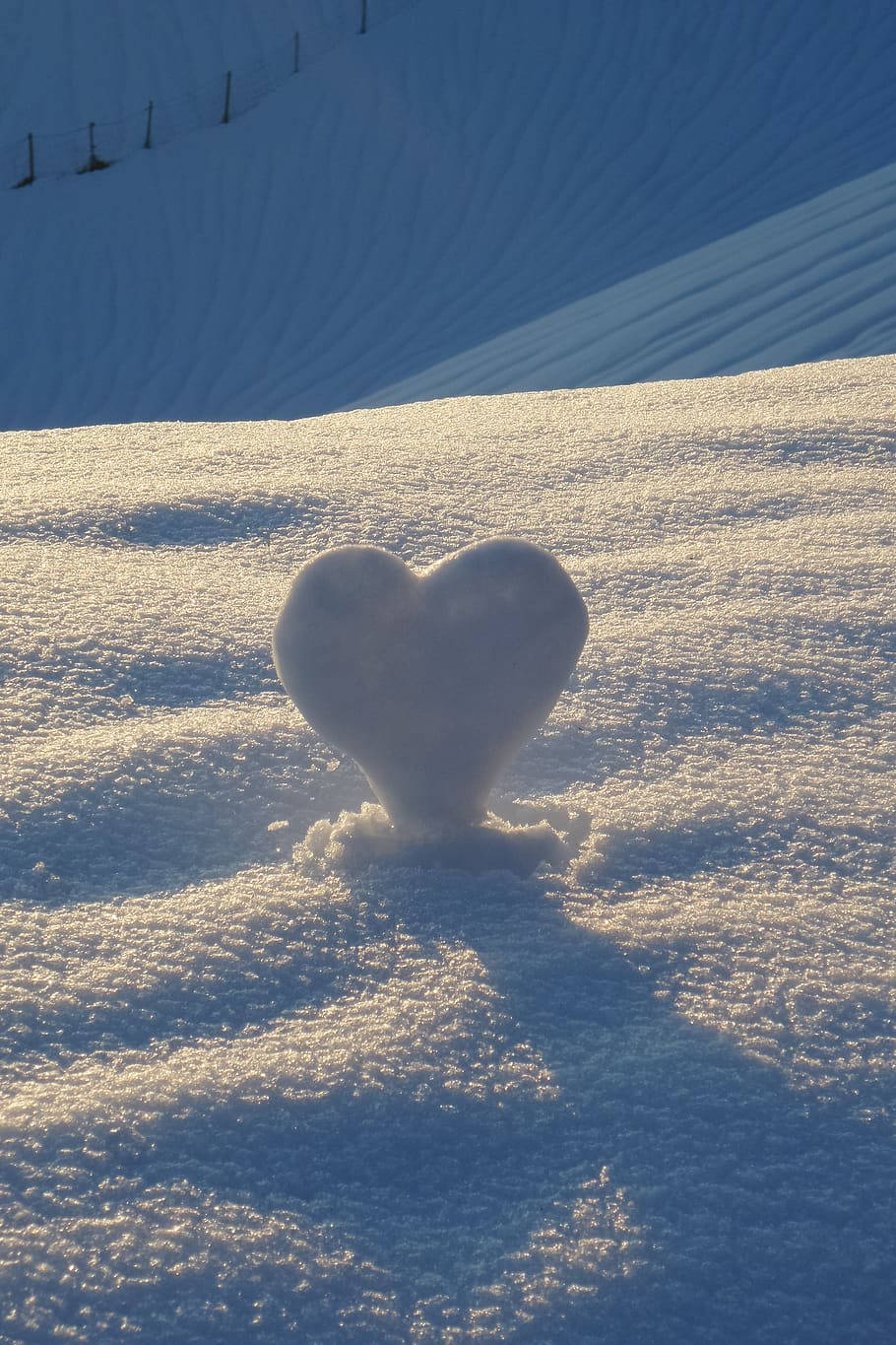 雪白心形 壁紙 — 一個心形雪雕在金色陽光下閃耀，背景是白雪覆蓋的斜坡和修整過的滑雪道。