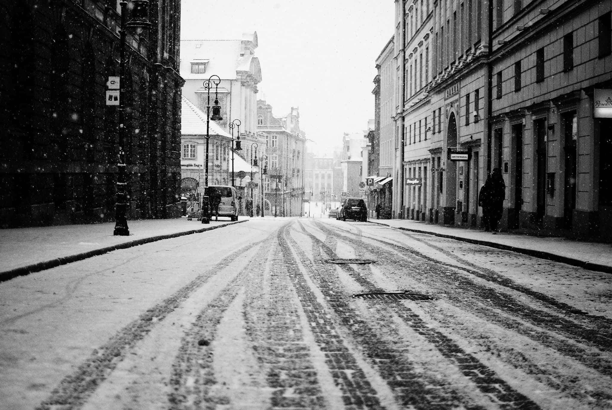 Black And White Street 桌布 壁紙 — 雪花飄落在灰濛濛的冬日天空下，一條由歷史悠久的歐洲建築環繞的寧靜鵝卵石街道上。