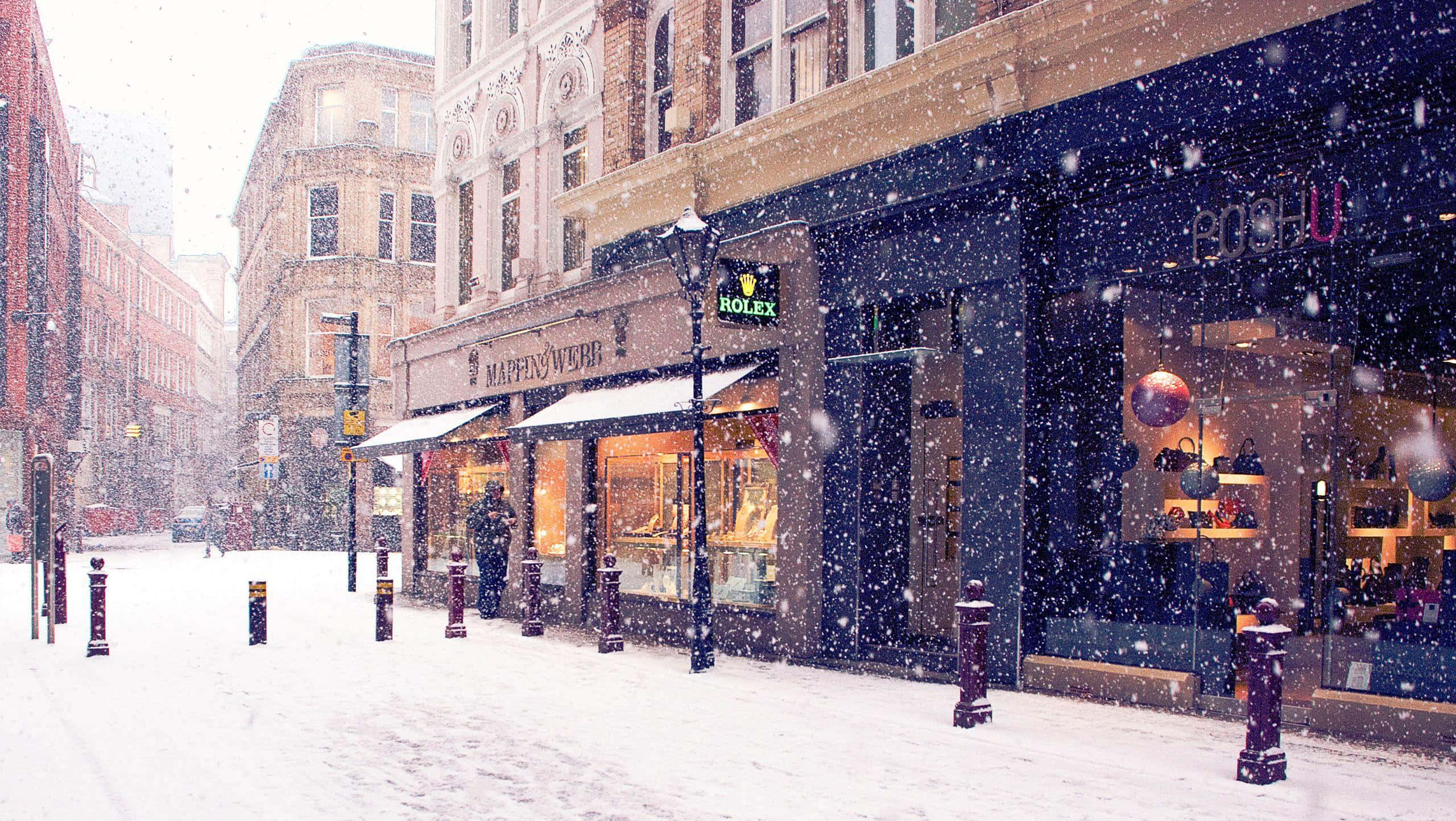Winter Cityscape 桌布 壁紙 — 雪花飄過一條寧靜的城市街道，兩旁是歷史建築和閃爍的商店櫥窗。