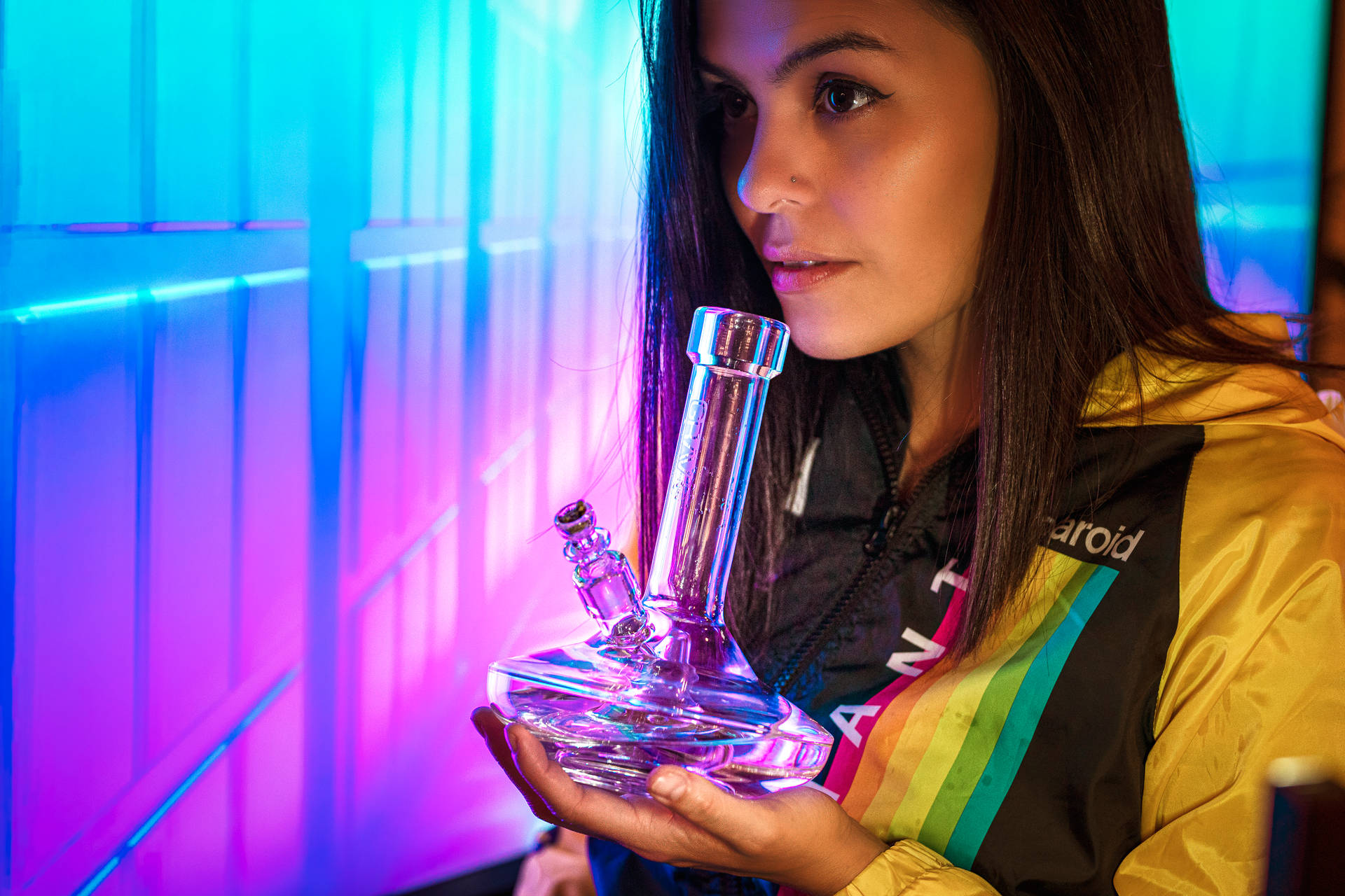 女性在霓虹燈房間裡手持玻璃水煙槍，穿著彩虹外套。