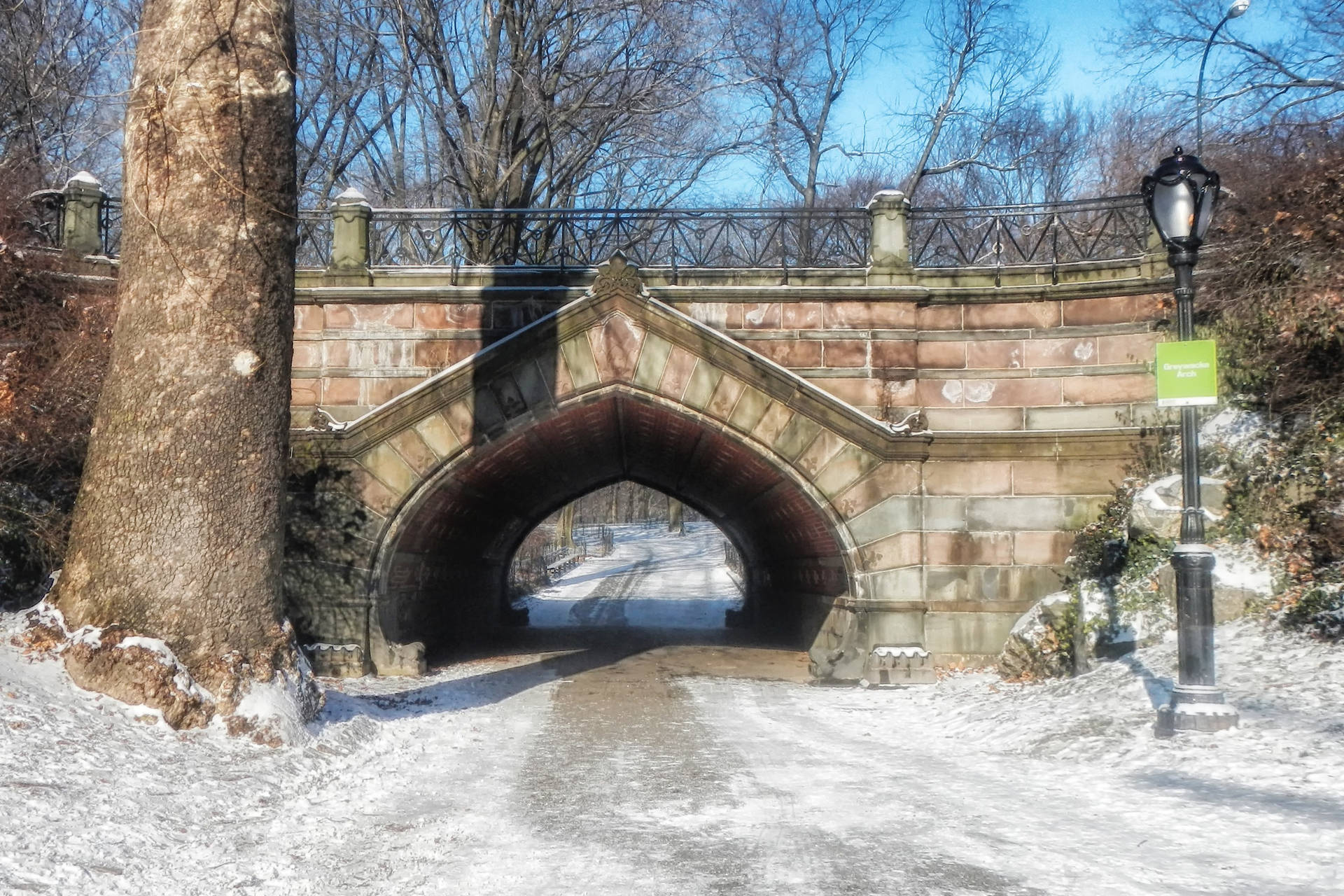 雪地公園中的石拱橋，光禿禿的樹木和路燈。