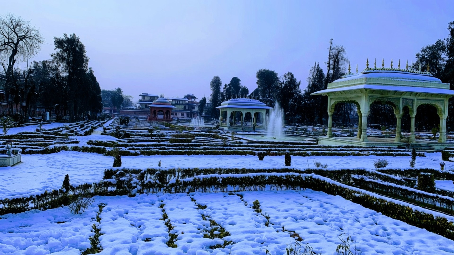 雪覆蓋著帶有亭閣和噴泉的正式花園，在暮色中。
