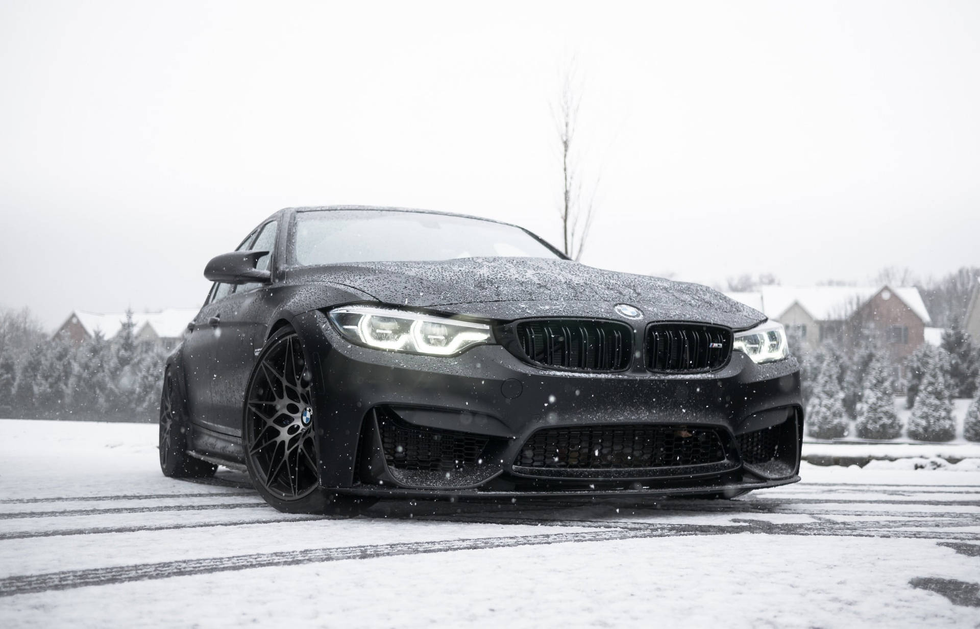 黑色BMW M4在雪中飄移，背景有積雪的房屋和樹木。