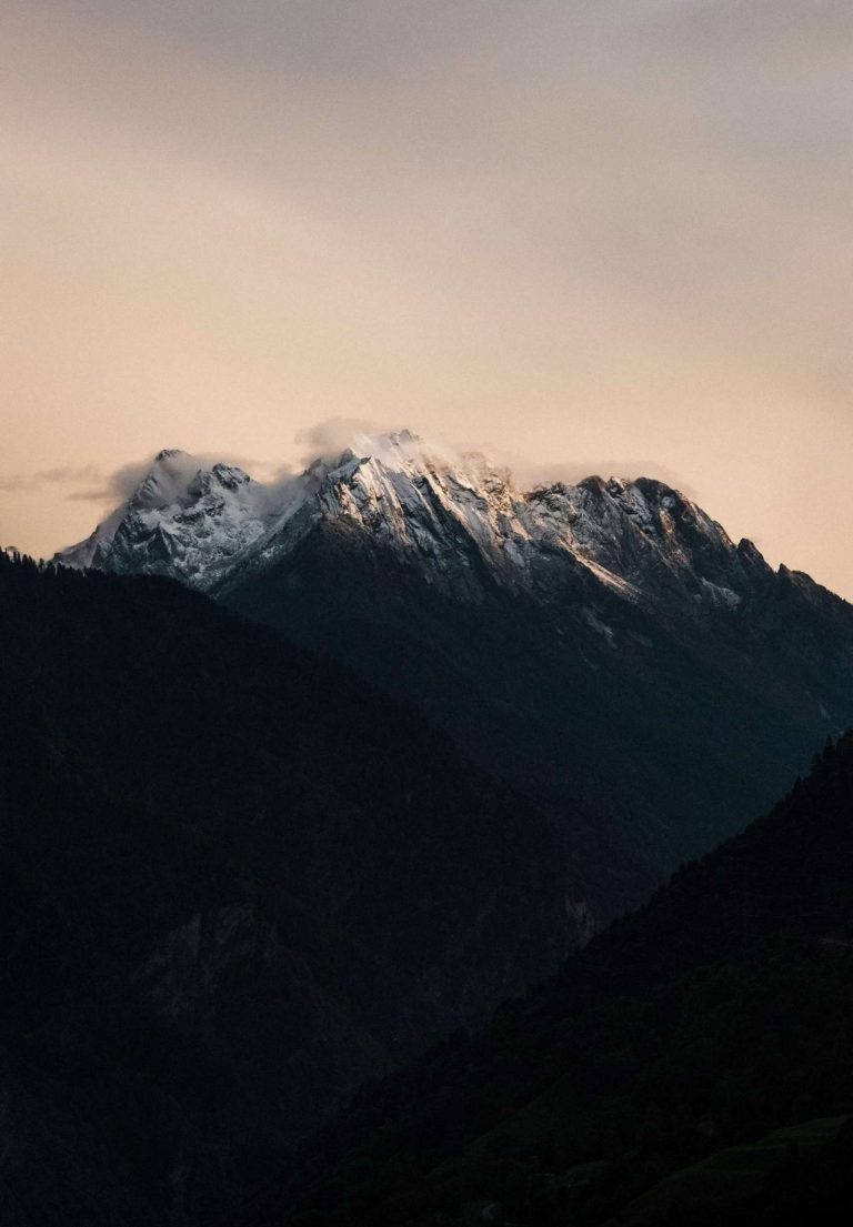 白雪覆蓋的山峰在黃昏時分發光，雲朵飄過山脊。
