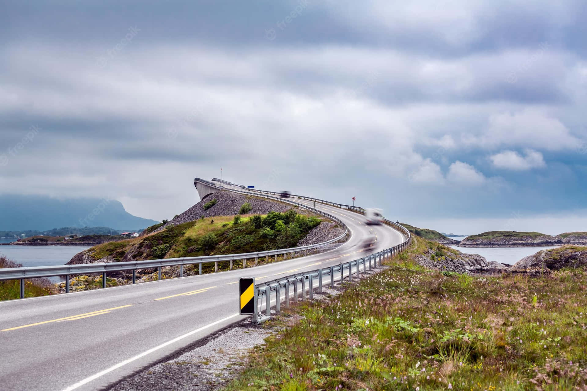 多雲天空下蜿蜒的海岸道路，有山脈和水域