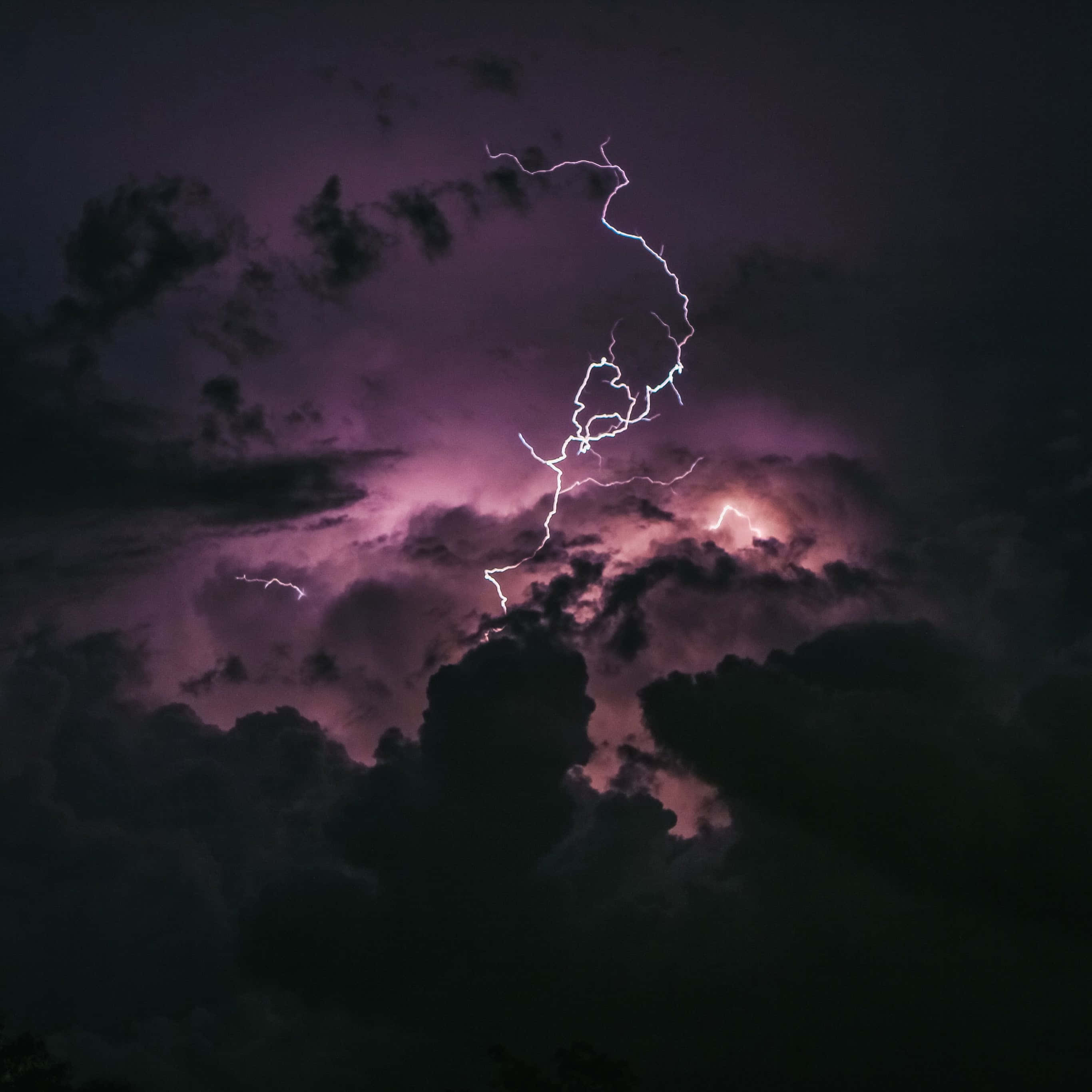 雲層中的閃電 壁紙 — 一道鋸齒狀閃電在洶湧的紫色暴風雨天空中分叉，照亮濃密的雲層，形成戲劇性的夜間景象。