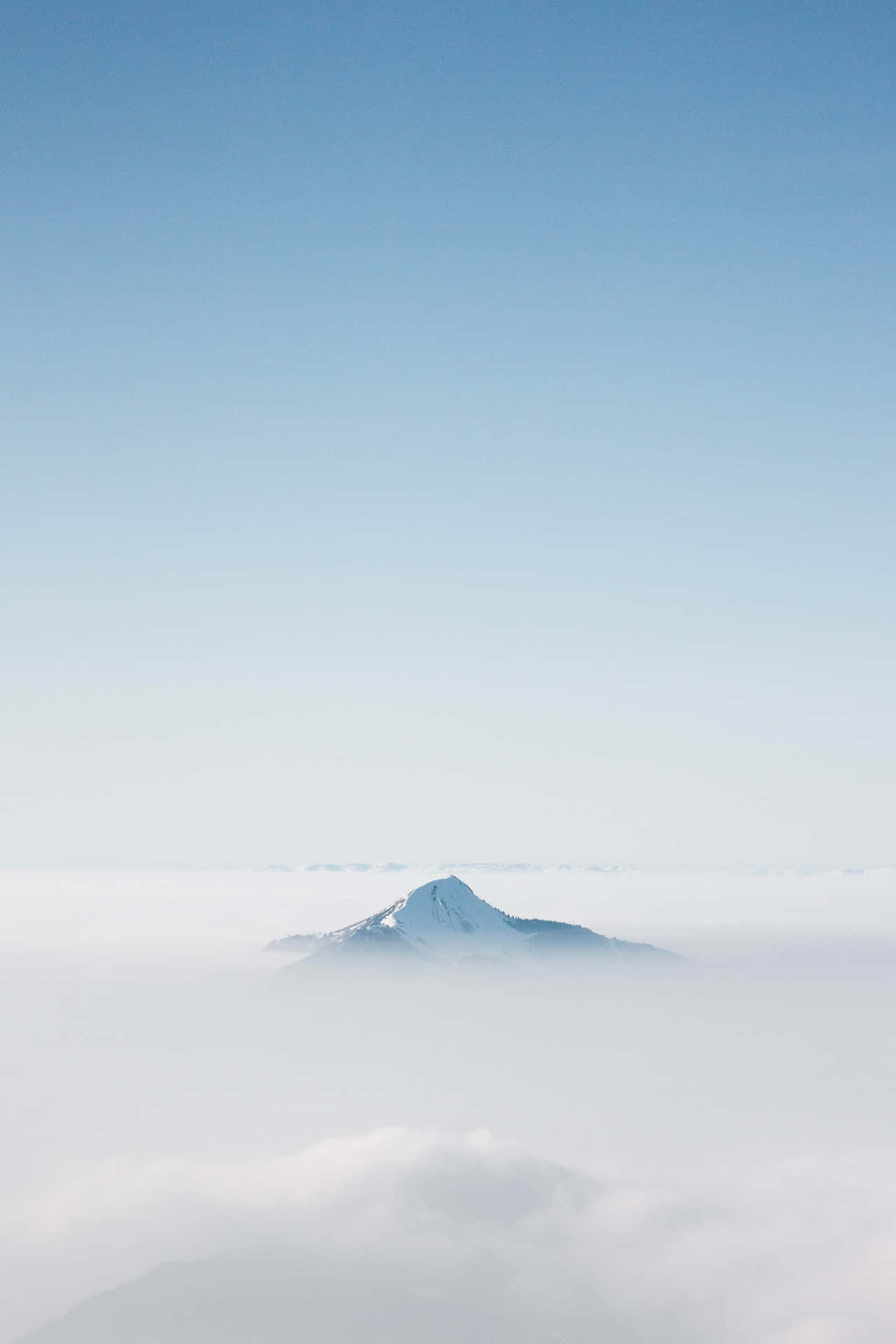 白雪覆蓋的山峰在清澈的藍天下從雲層中浮現。