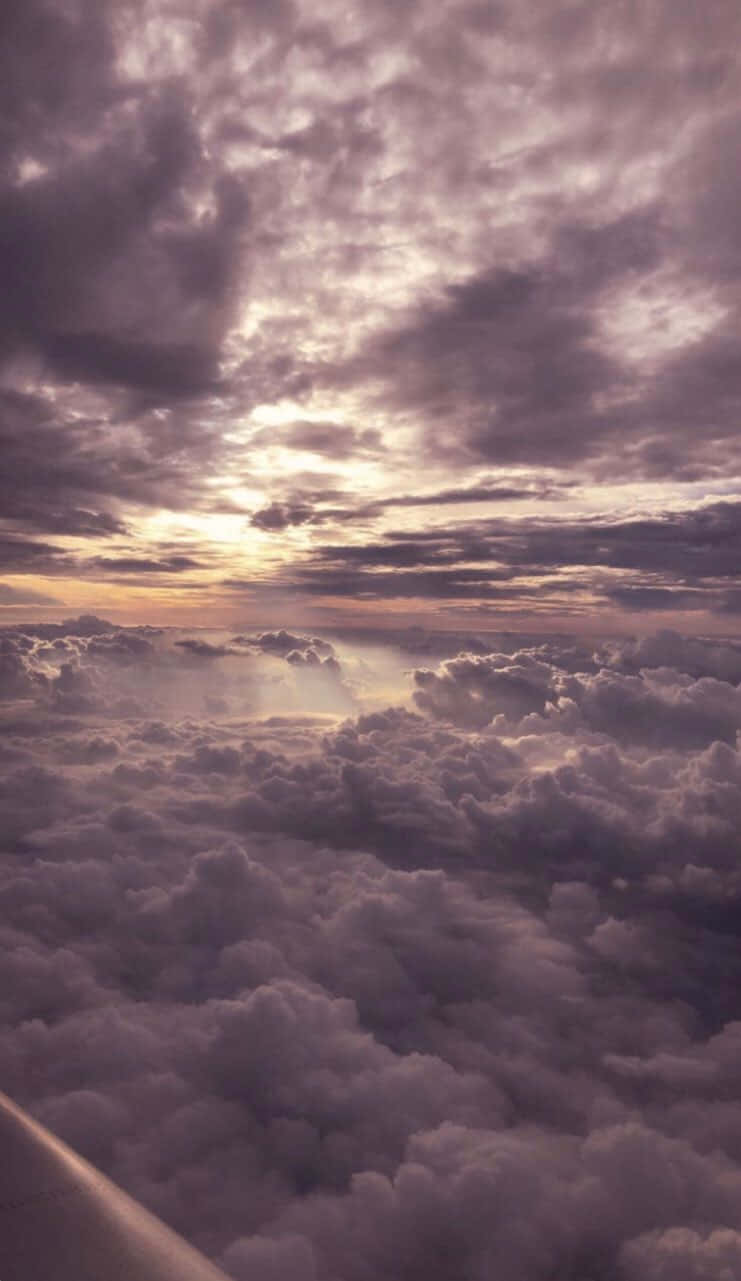 雲層之上日落空拍 壁紙 — 從空中俯瞰蓬鬆雲朵沐浴在金色夕陽光中，帶有紫色和橙色色調。