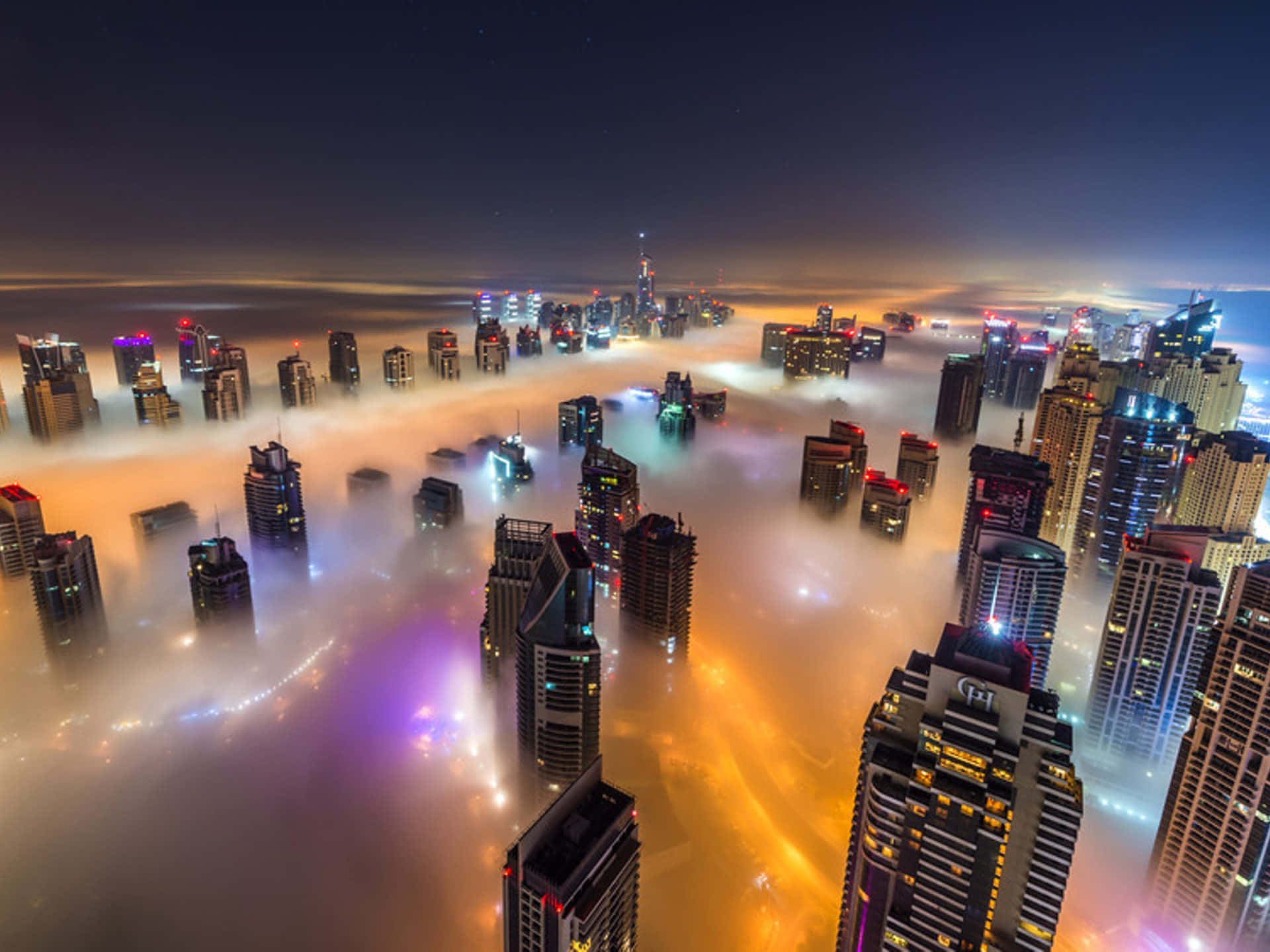 雲層之上的城市夜景 壁紙 — 摩天大樓在夜間穿透發光的橙色和紫色霧氣的鳥瞰圖，上方有星空。