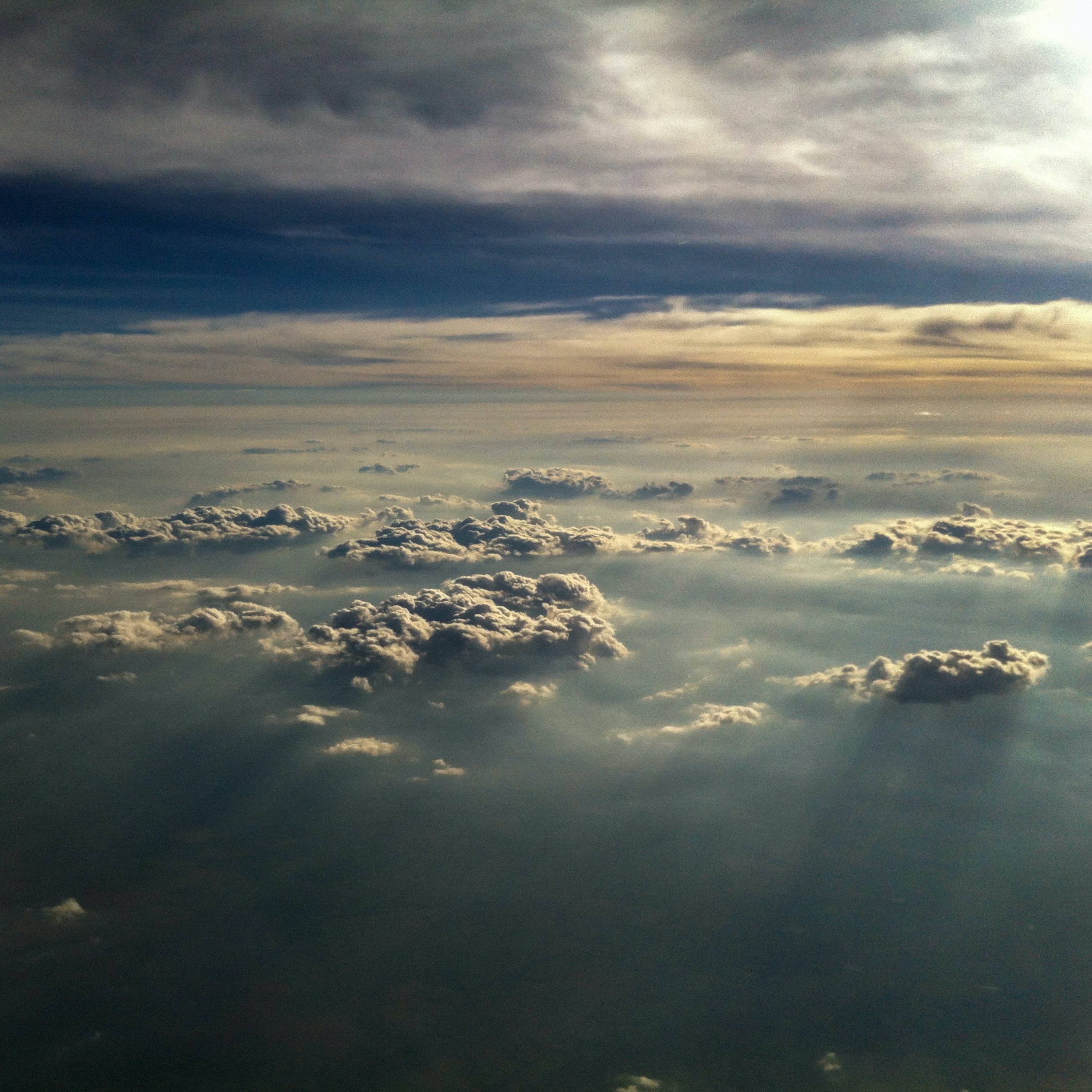 雲層之上的美麗天空 壁紙 — 陽光穿過層層雲層，在下方廣闊的海洋上投射出金色的光芒。