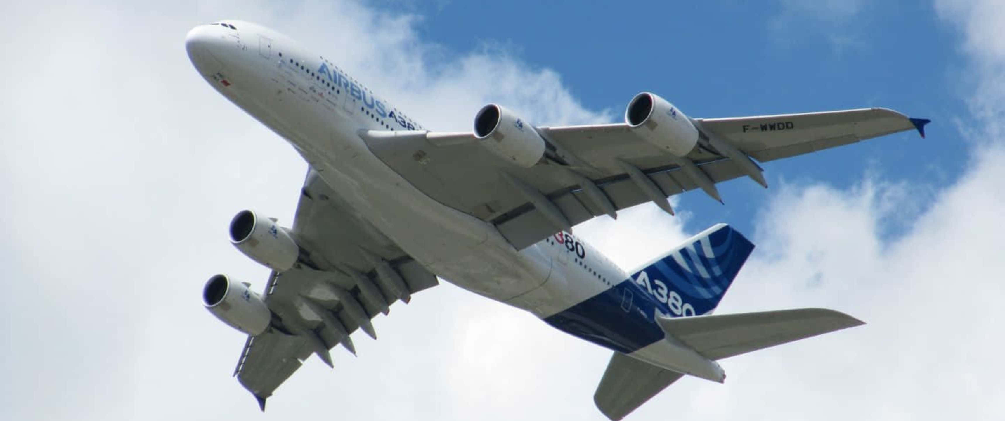 雲層密布的巨型客機 3440x1440p 背景 壁紙 — 一架巨大的空中巴士A380飛機在點綴著蓬鬆白雲的明亮藍天中翱翔。