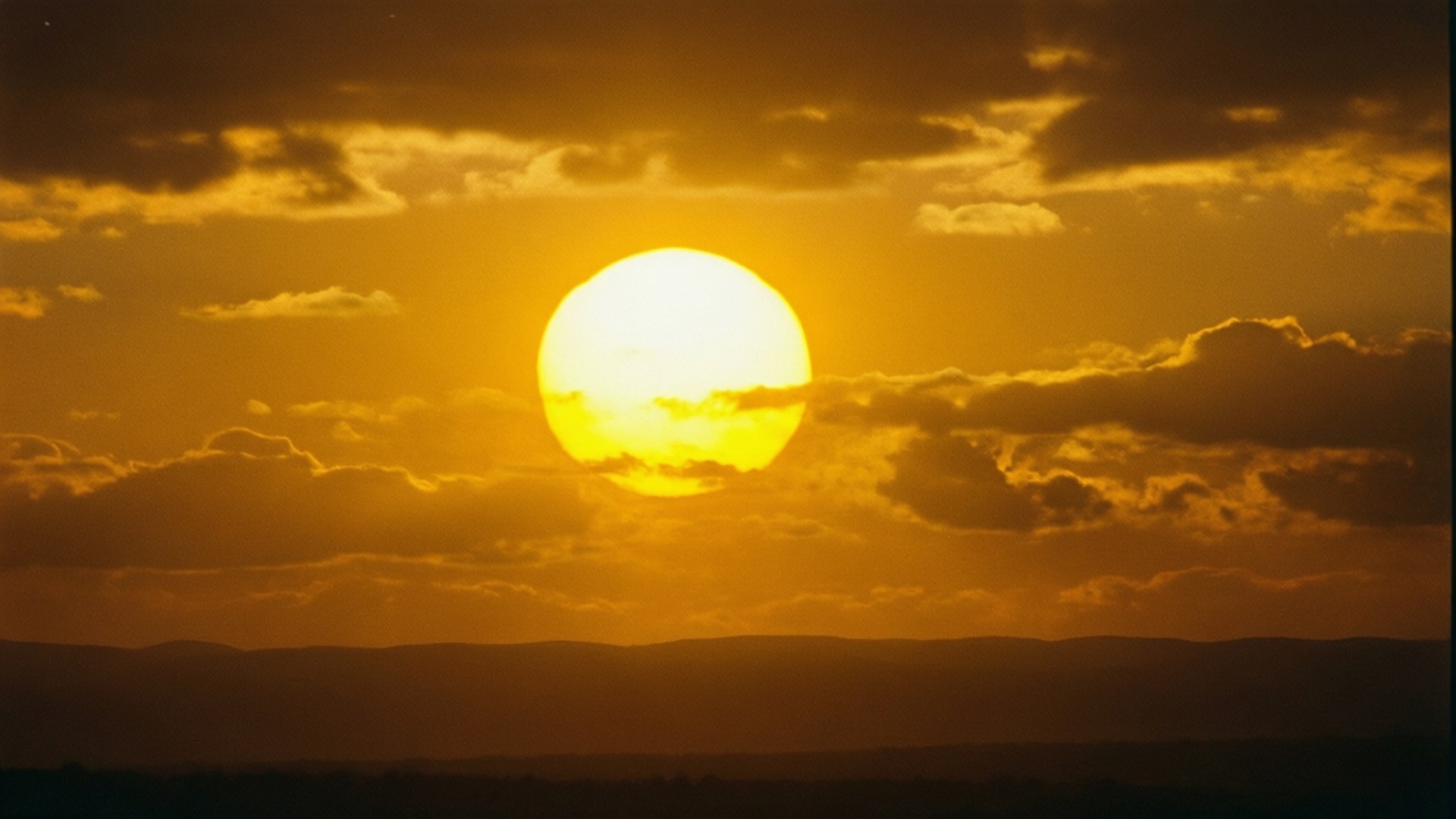金色夕陽在雲層後落下，映照著黑暗的山丘