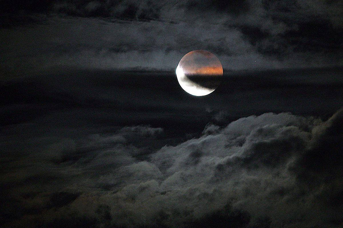 雲層月食 壁紙 — 血月在黑暗雲層中發光，伴隨著旋轉的灰色和黑色雲層，構成戲劇性的夜空。