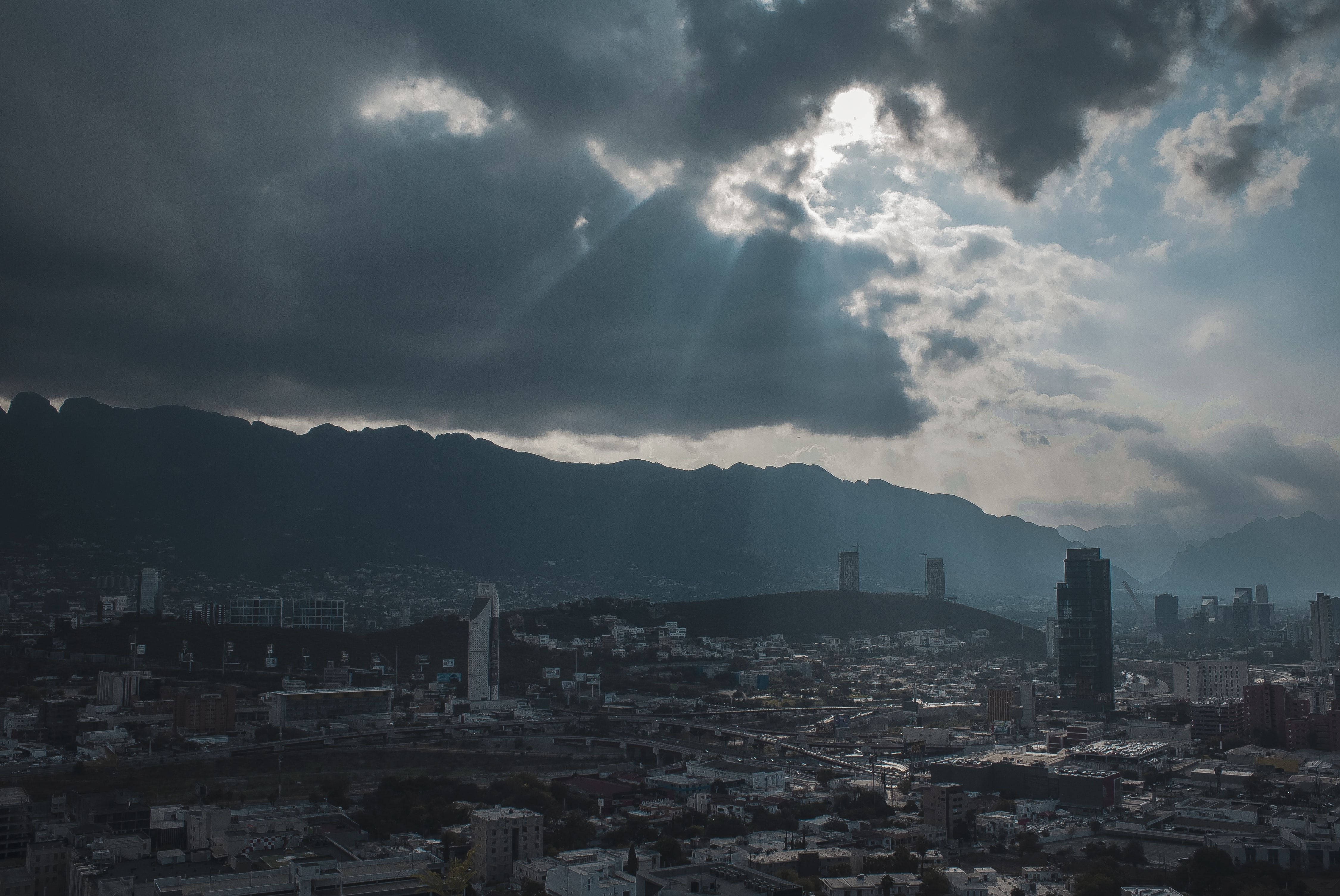 雲層籠罩下的蒙特雷市 壁紙 — 戲劇性的陽光穿透黑暗的暴風雲，照耀在依偎著陰影山脈的廣闊城市上。