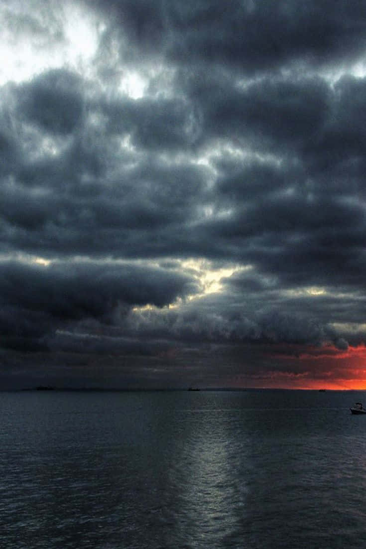 雲層繚繞的秋日美景 壁紙 — 戲劇性的暴風雲籠罩著平靜的海面，熾熱的日落色調從地平線滲透出來。